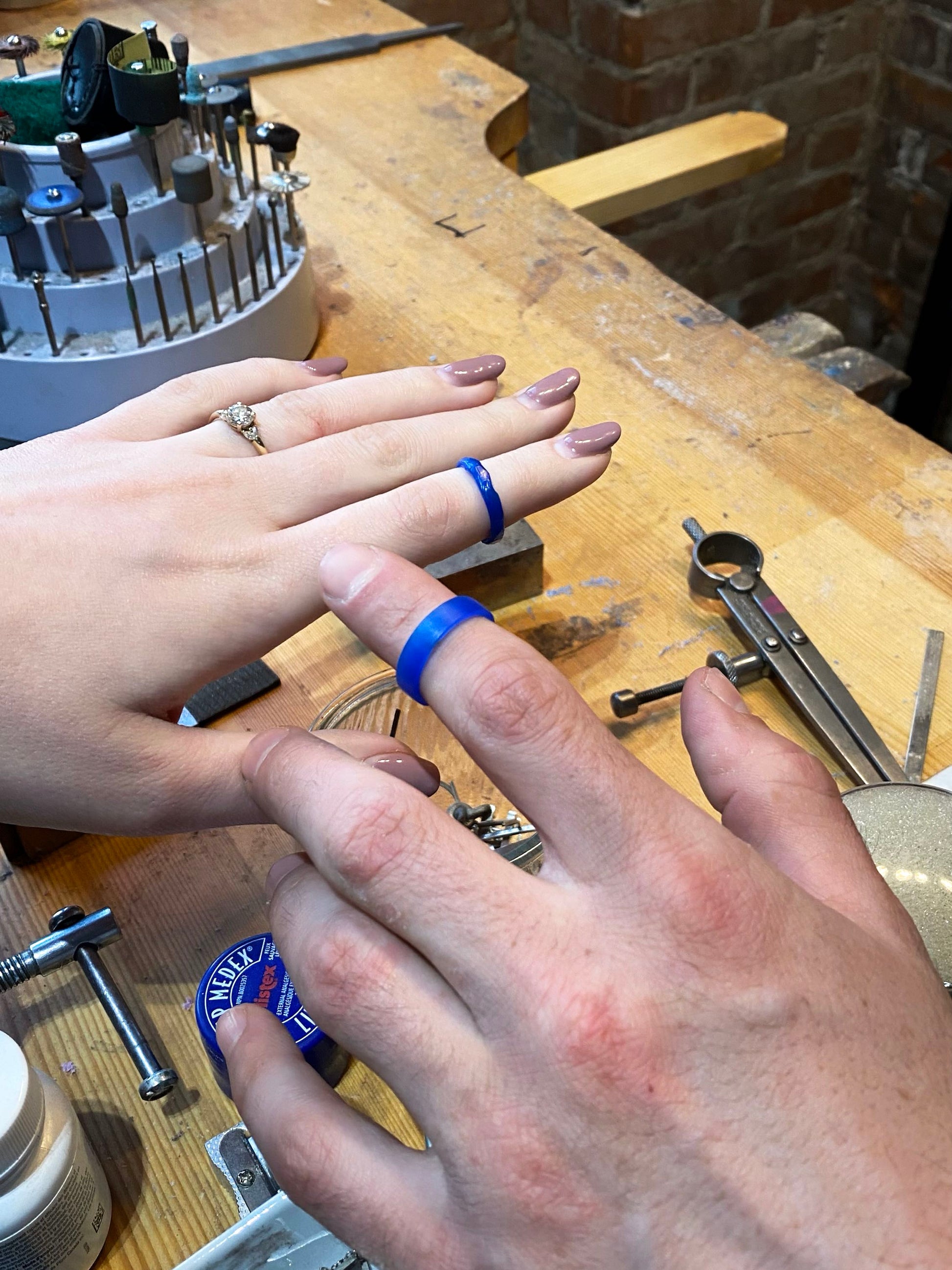 Two lost wax wedding ring models on hands on jewellery work bench