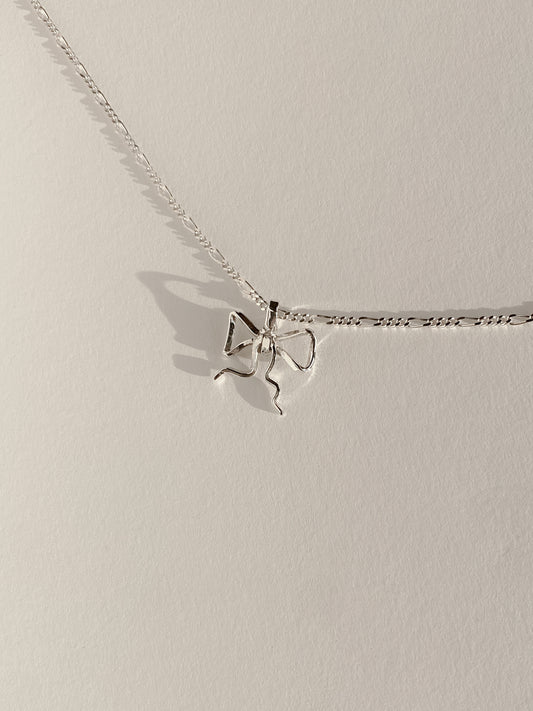 Silver bow pendant on multi link chain on white background