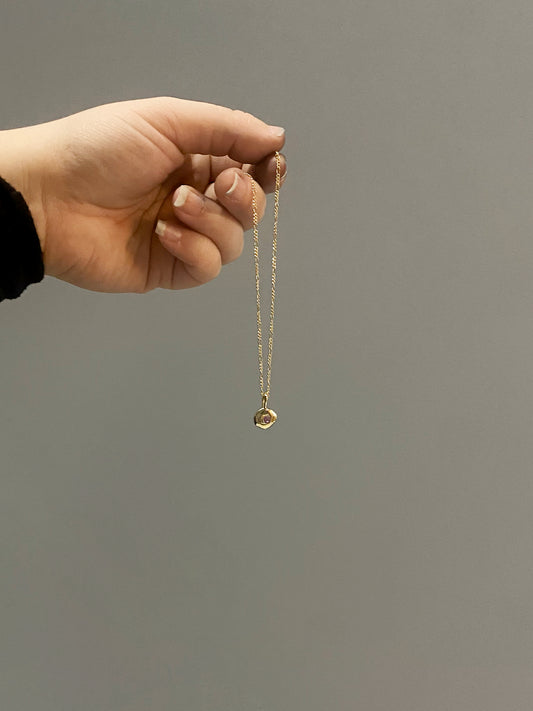Gold textured pendant with pink sapphire hanging on chain from hand