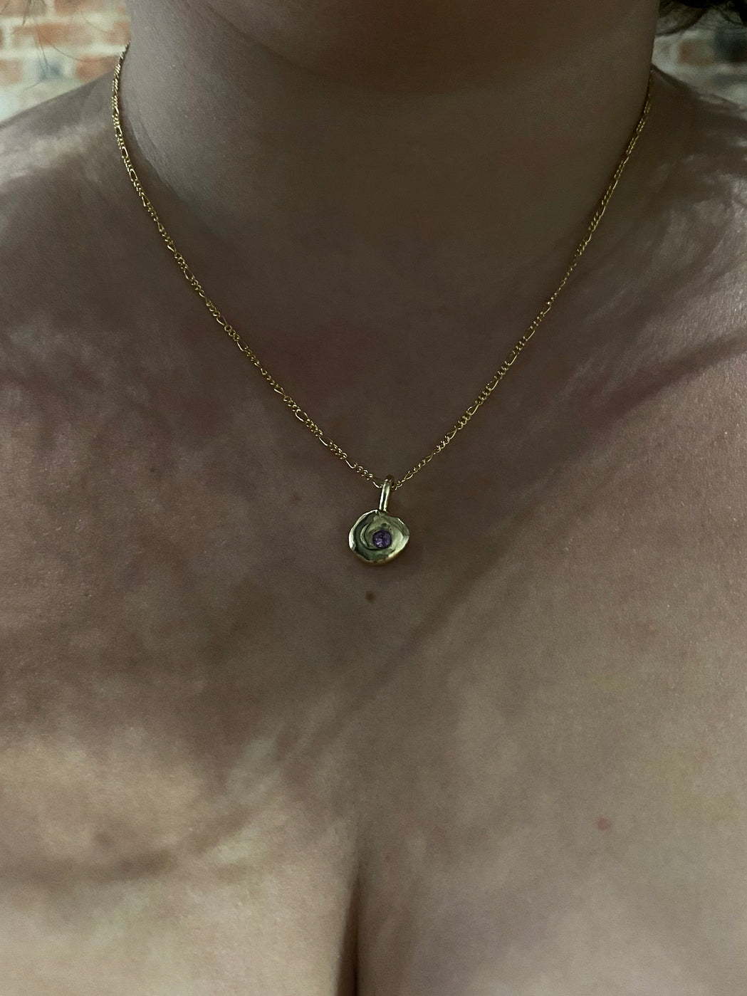 Gold textured pendant with pink sapphire hanging on chain on model