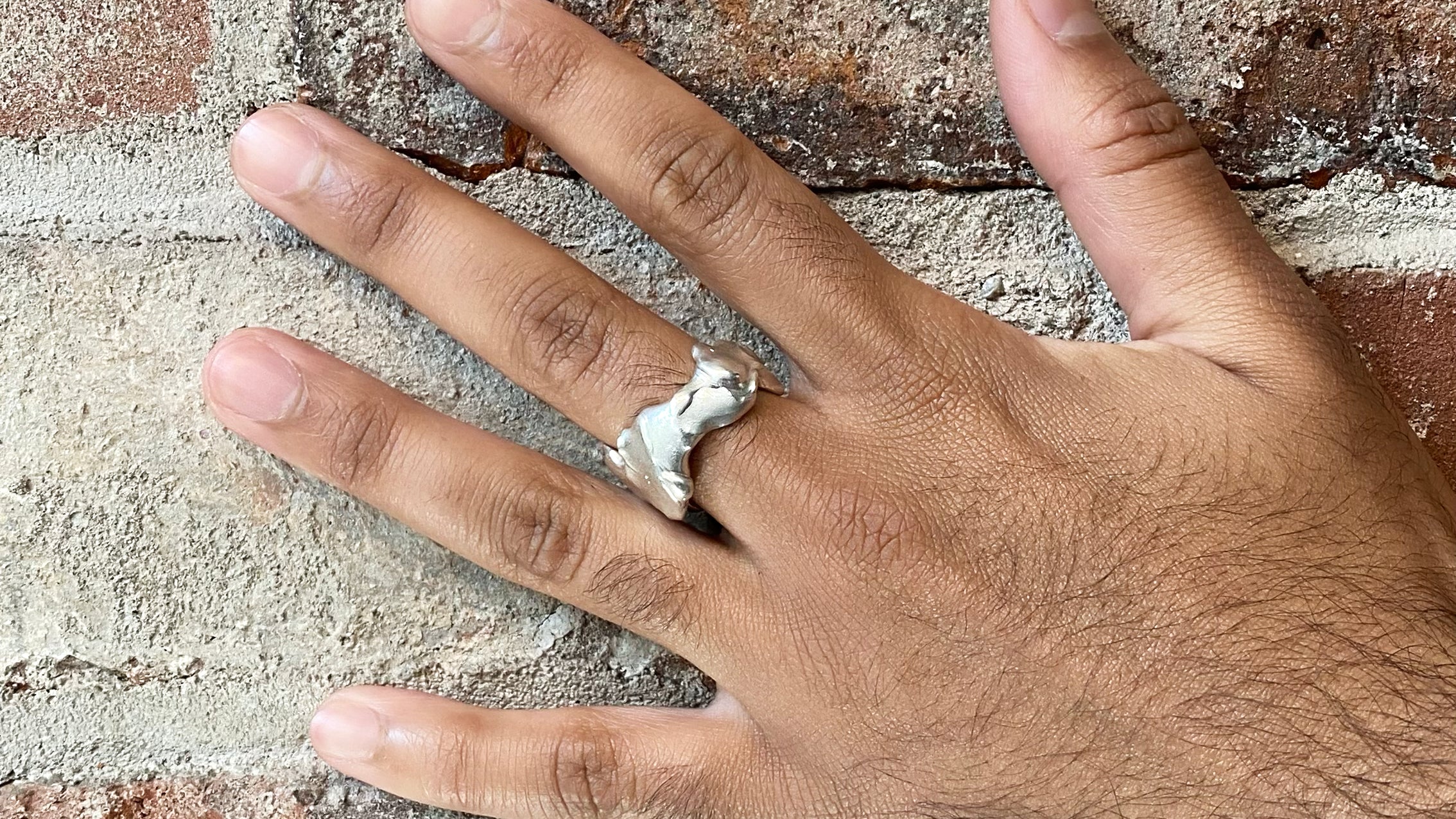 Textured silver ring on hand on brick background