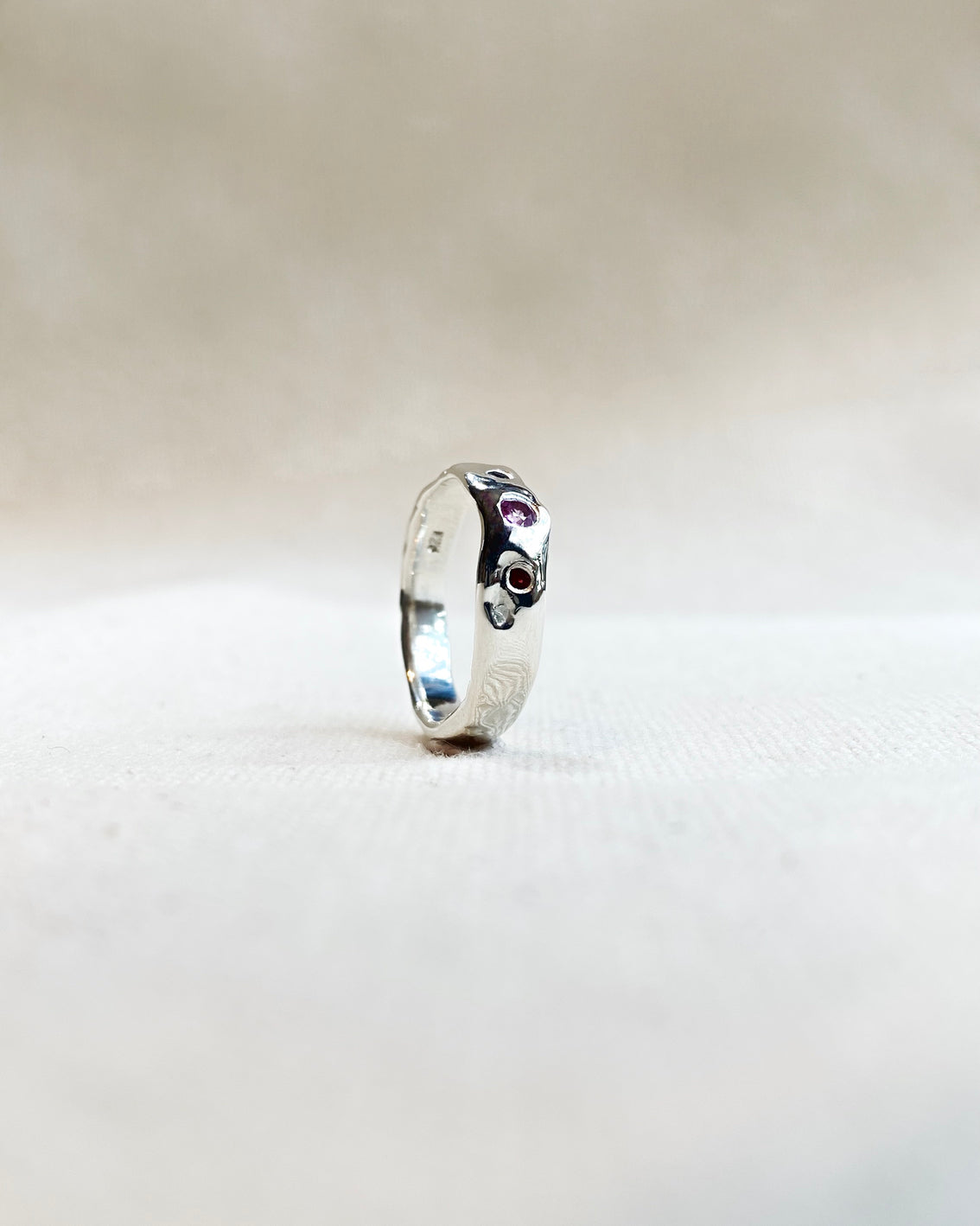 Molten silver ring with 1 blue, 1 red, and 1 pink sapphire on canvas