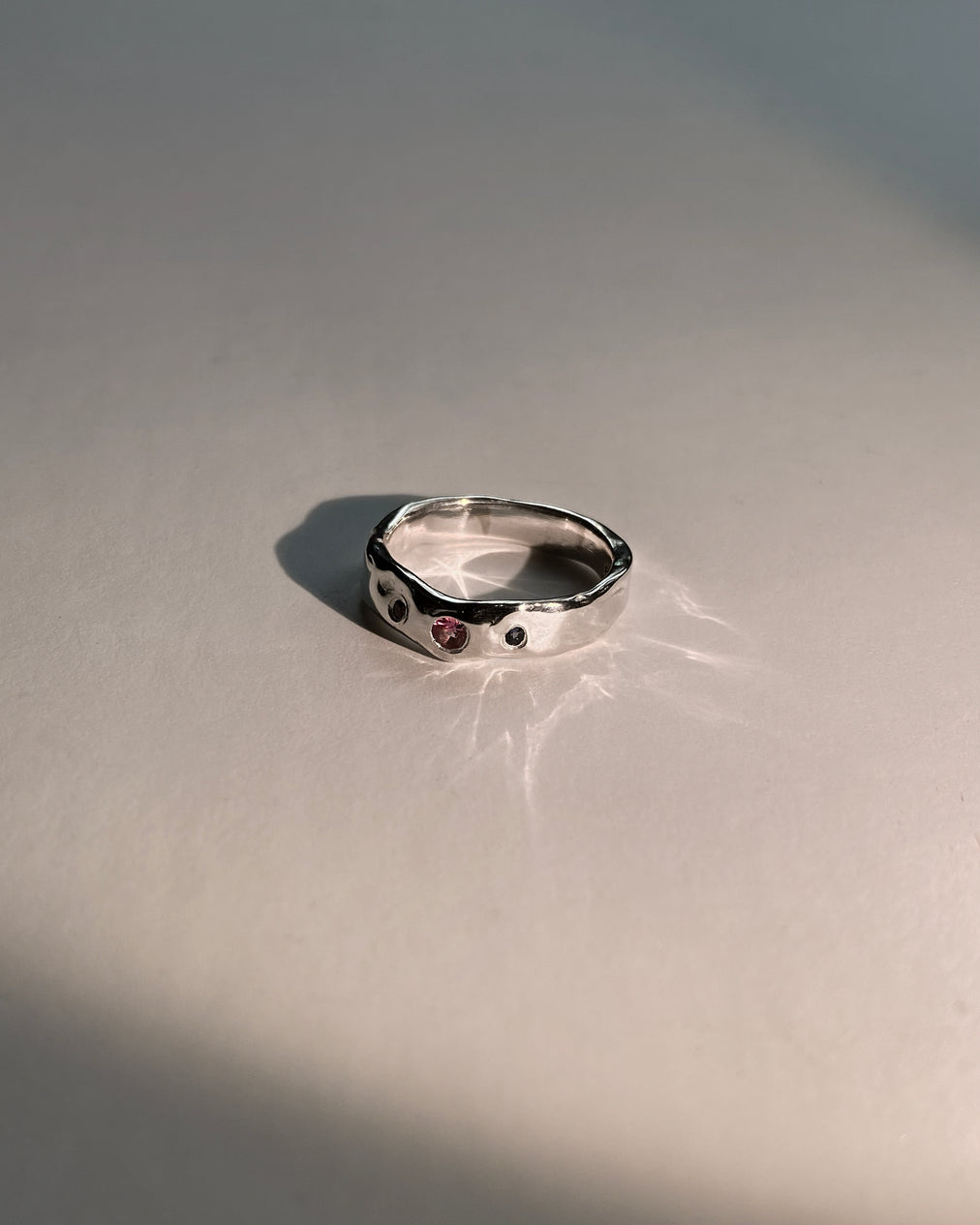 Molten silver ring with 2 blue and 1 pink sapphire on white background