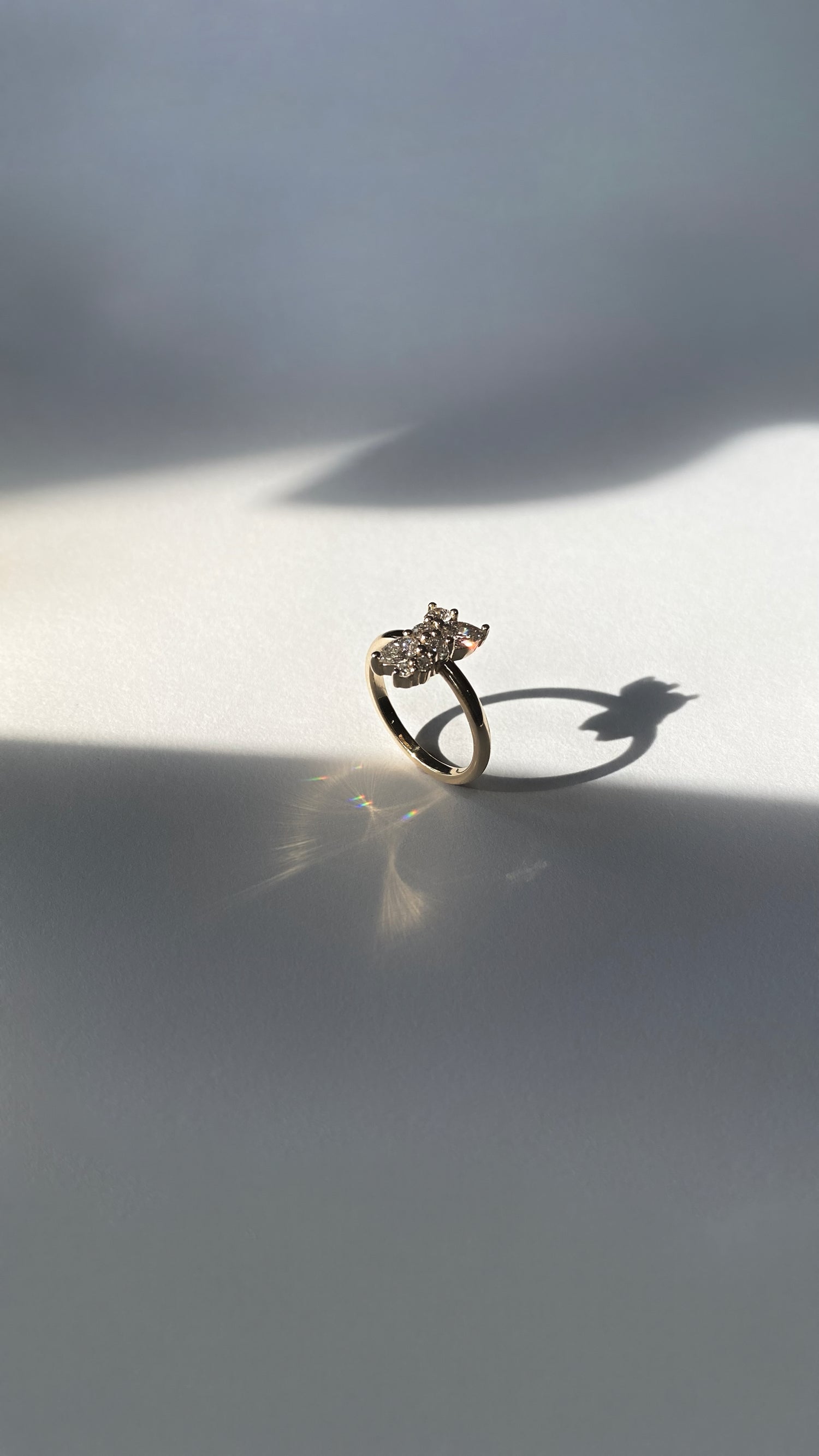 Gold ring with cluster of diamonds on white surface with shadows