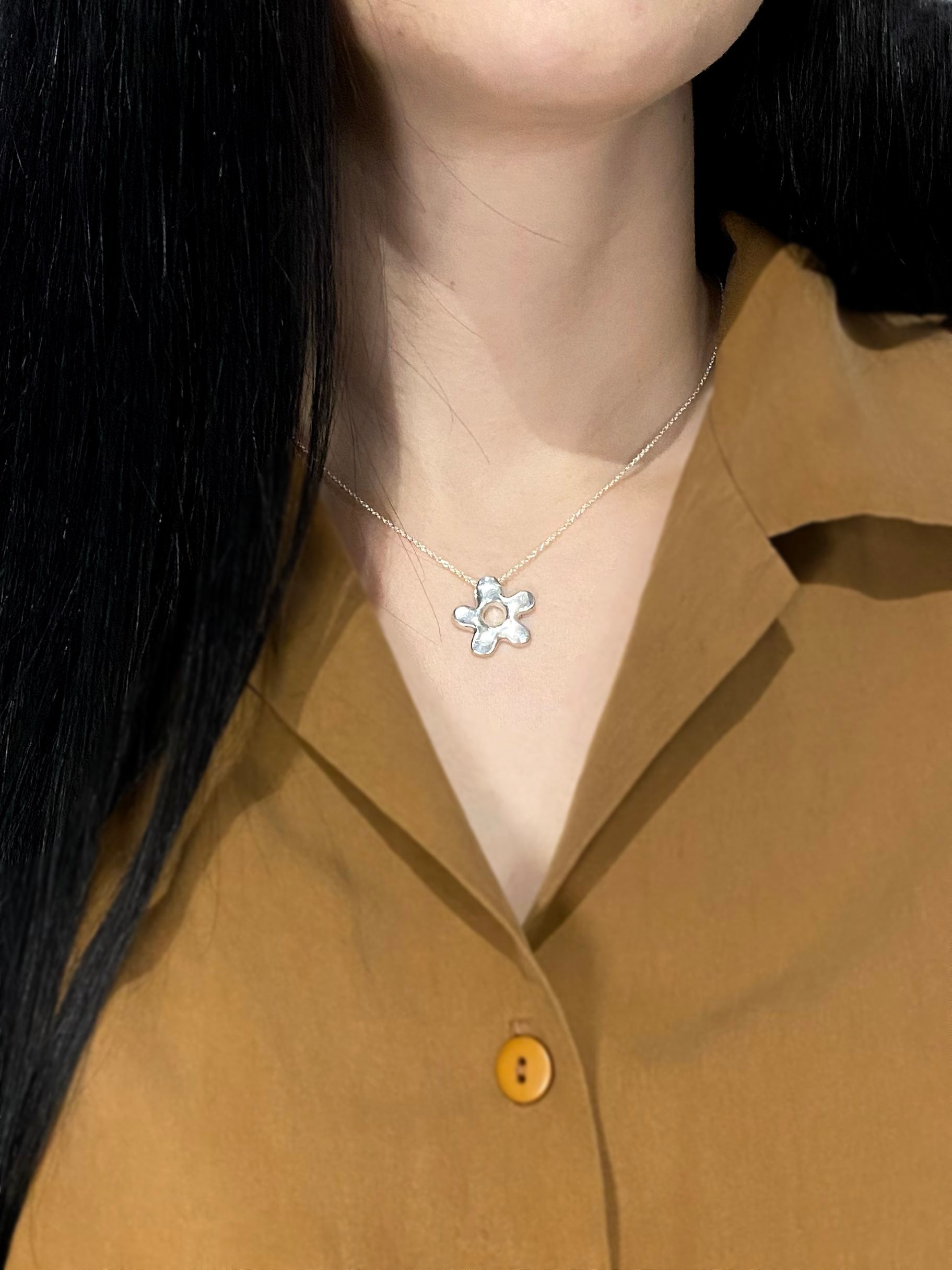 Silver daisy pendant on model with brown shirt and black long hair