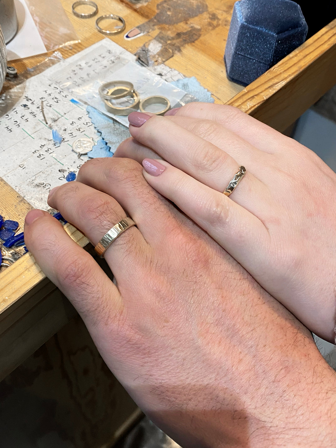 Two hands at work bench with their textured handmade wedding rings