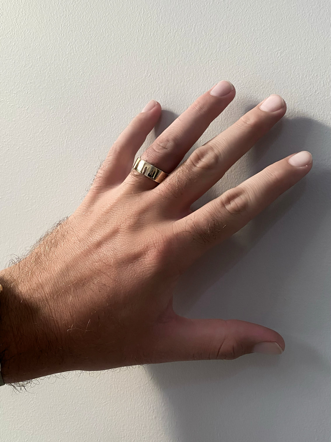 Hand with shiny yellow gold band at grey background