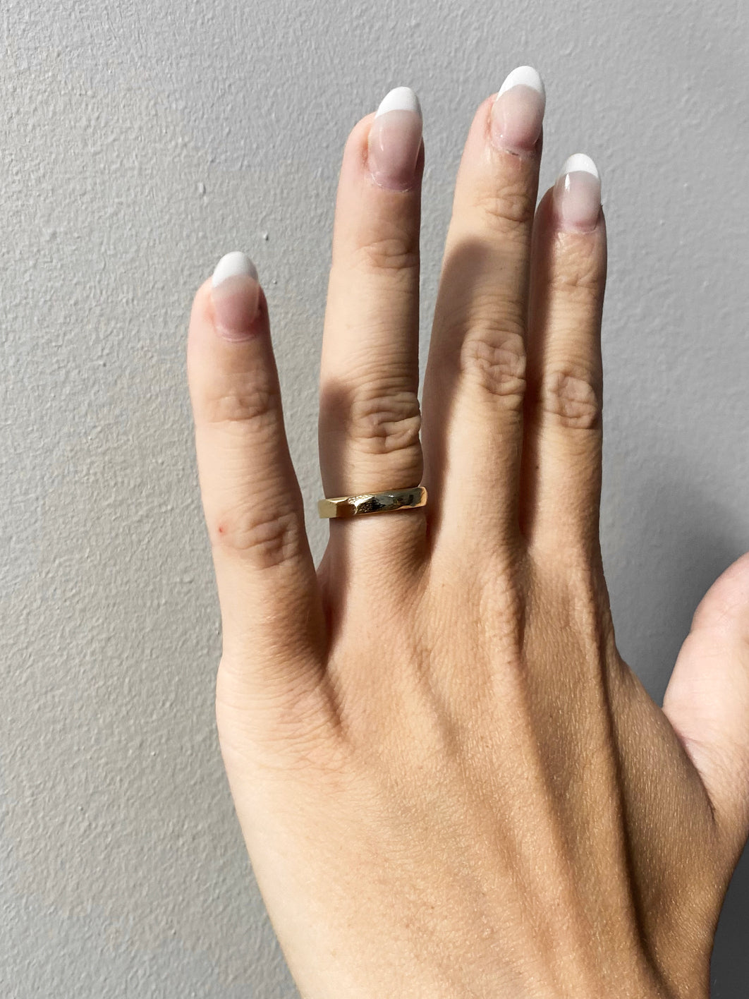 Hand with gold faceted wedding ring with grey background