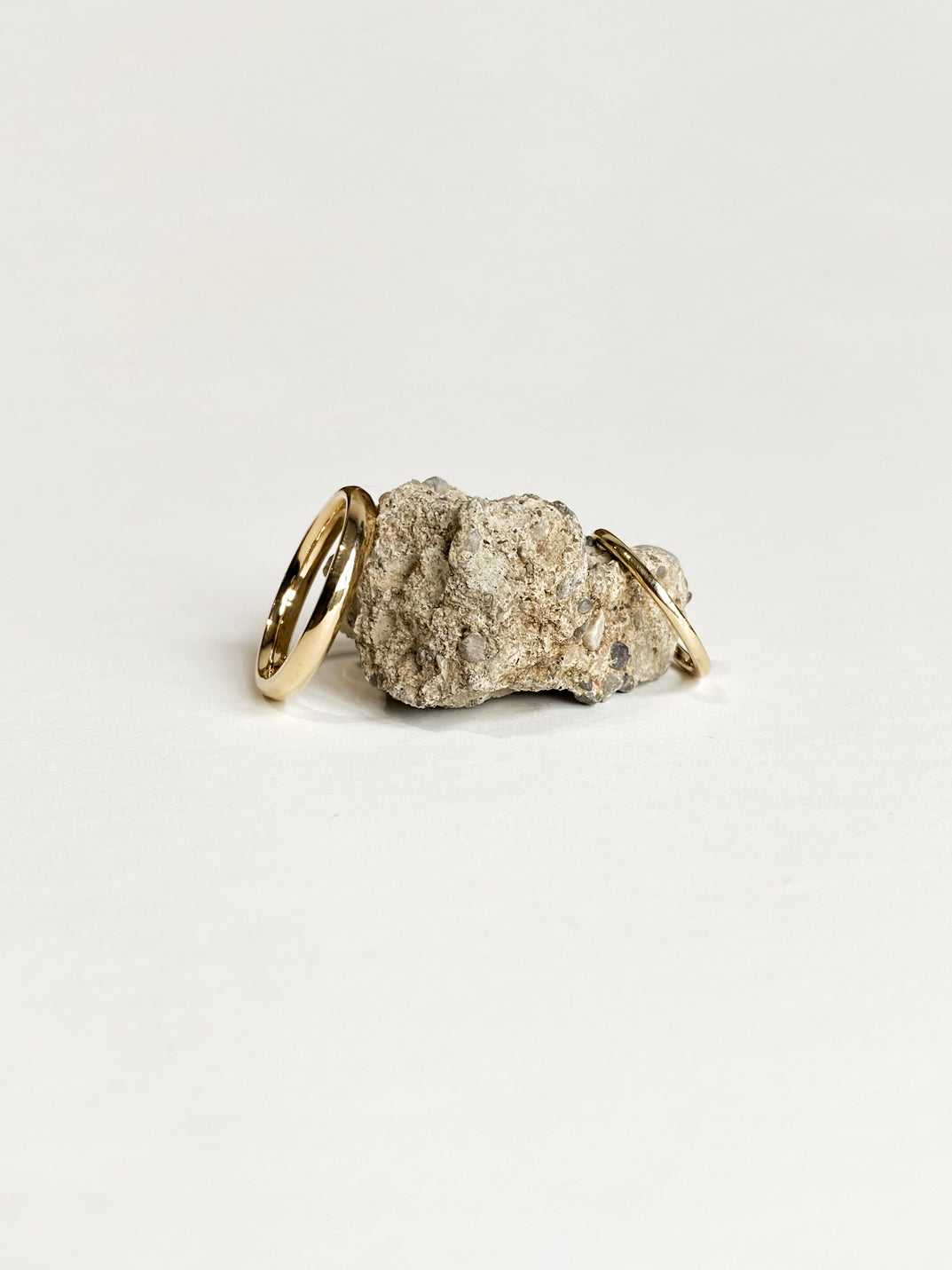 2 classic yellow gold wedding rings leaning against beige rock on white background