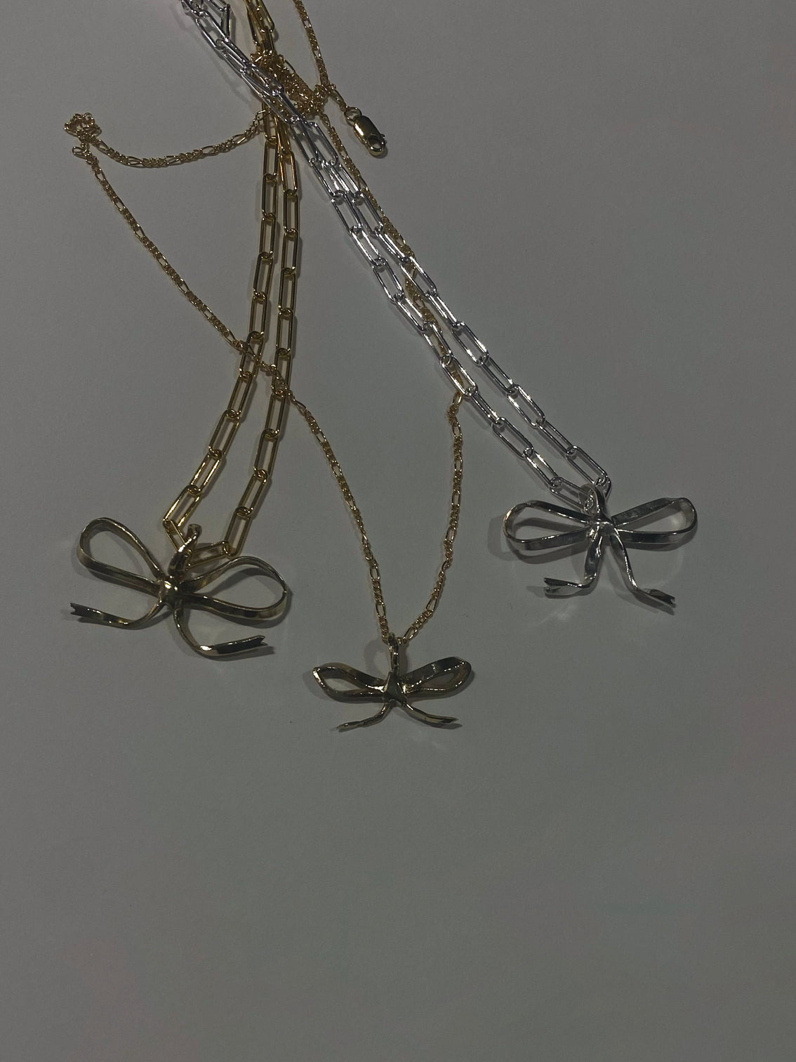 3 silver and gold bow pendants on grey background with tangled chains