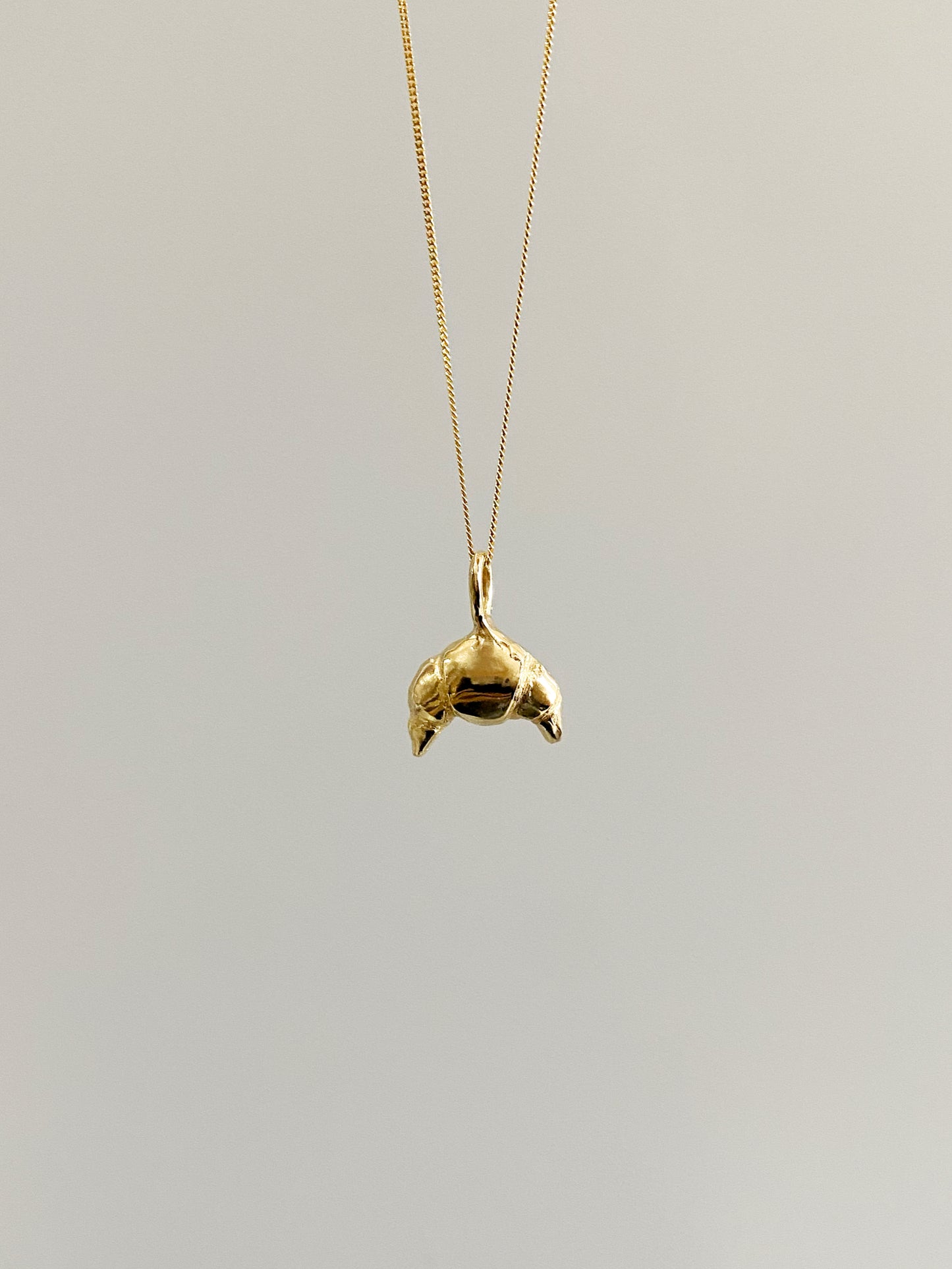 Gold croissant necklace on grey background