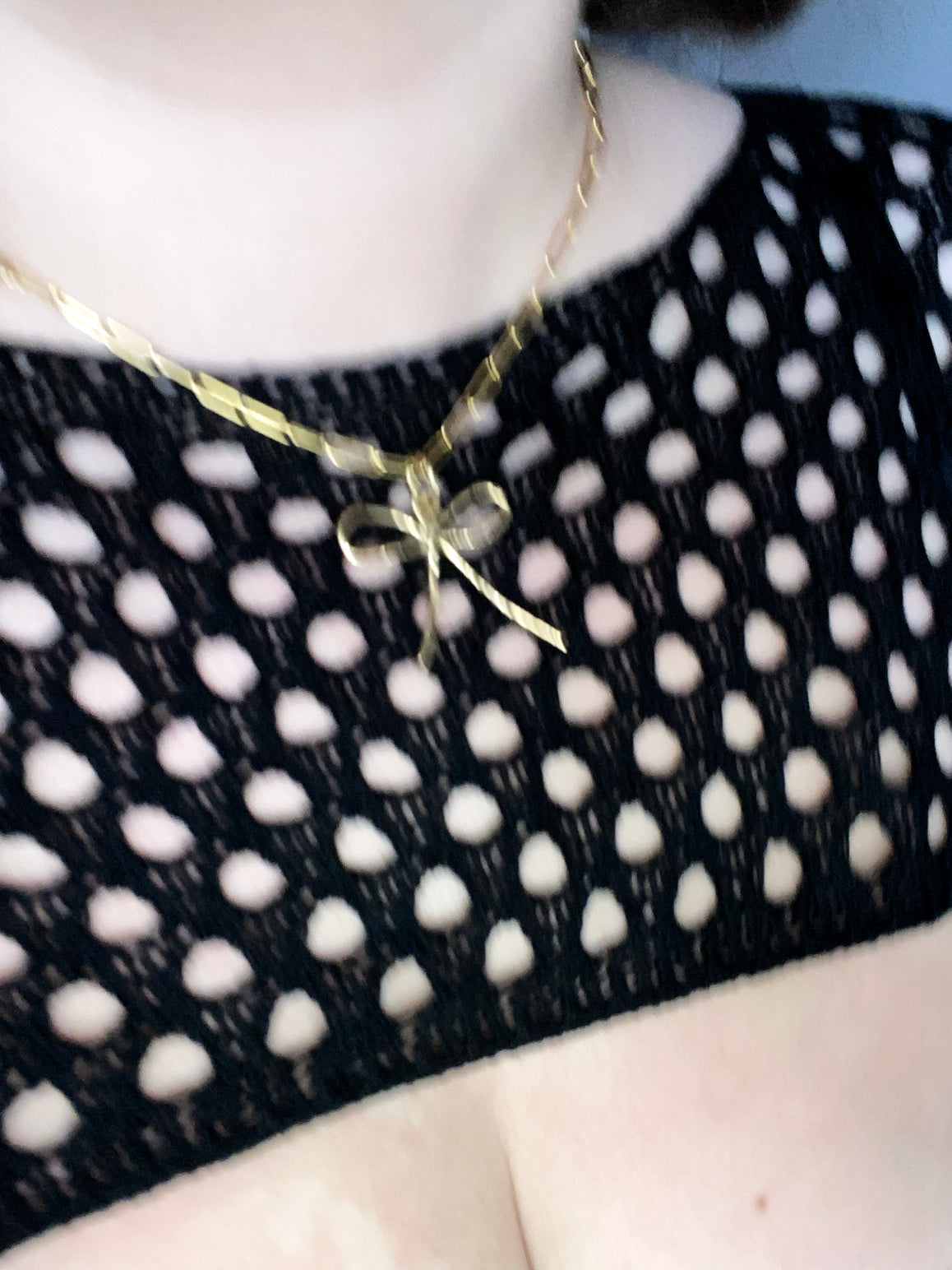 Gold bow pendant on large link chain on model with crochet black sweater