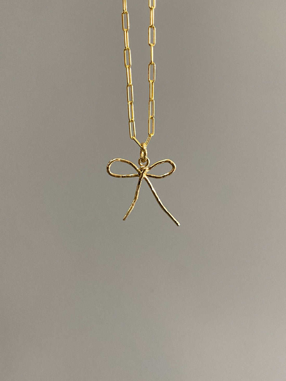Gold bow pendant on large link chain with grey background