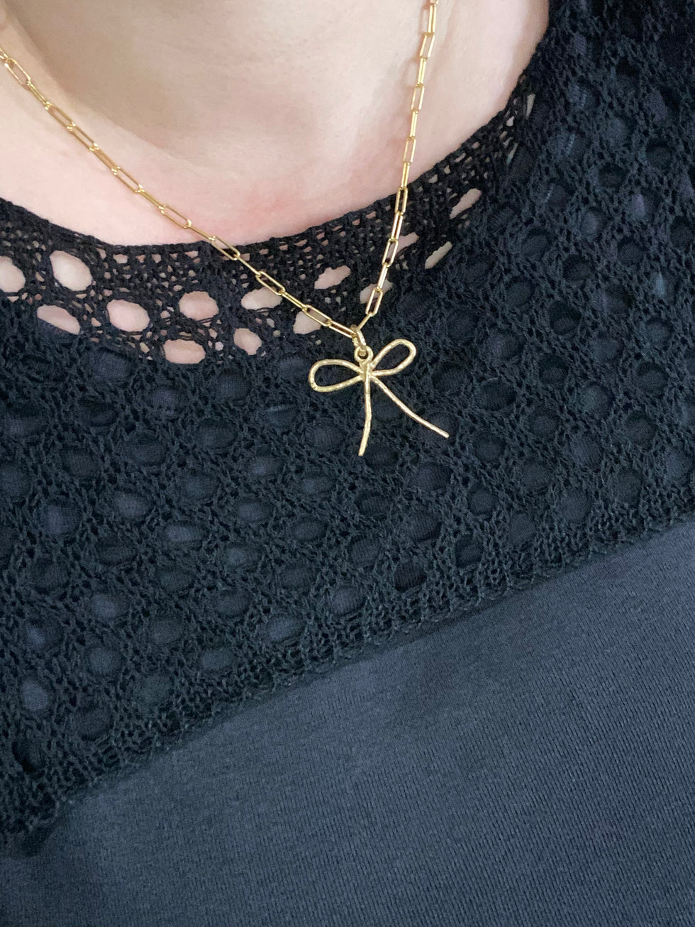 Gold bow pendant on large link chain on model with black sweater