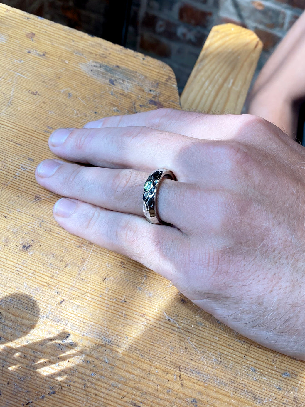 Hand on work table with white gold textured wedding ring 