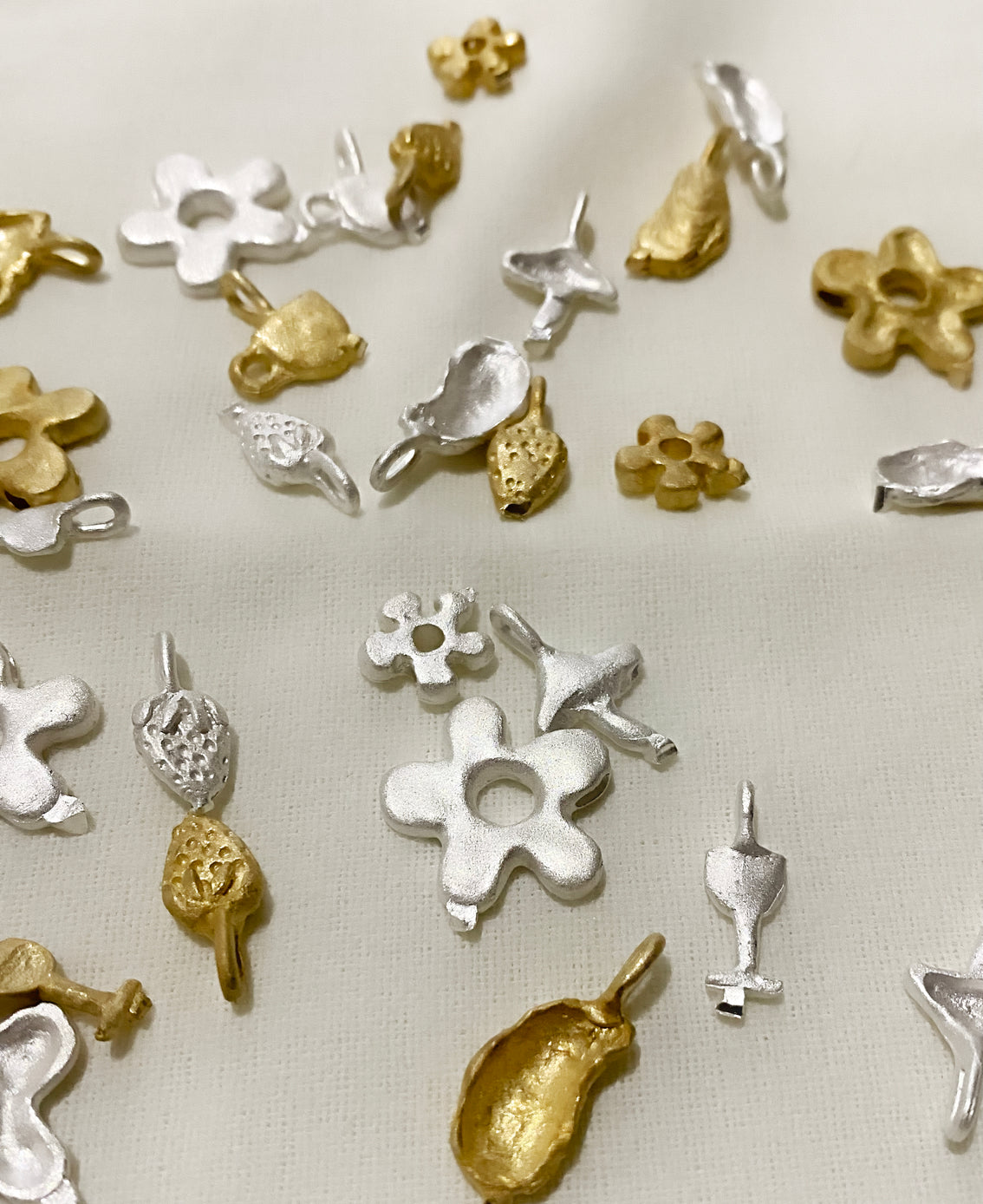 Raw silver and gold charm castings of mushrooms, flowers, and shells