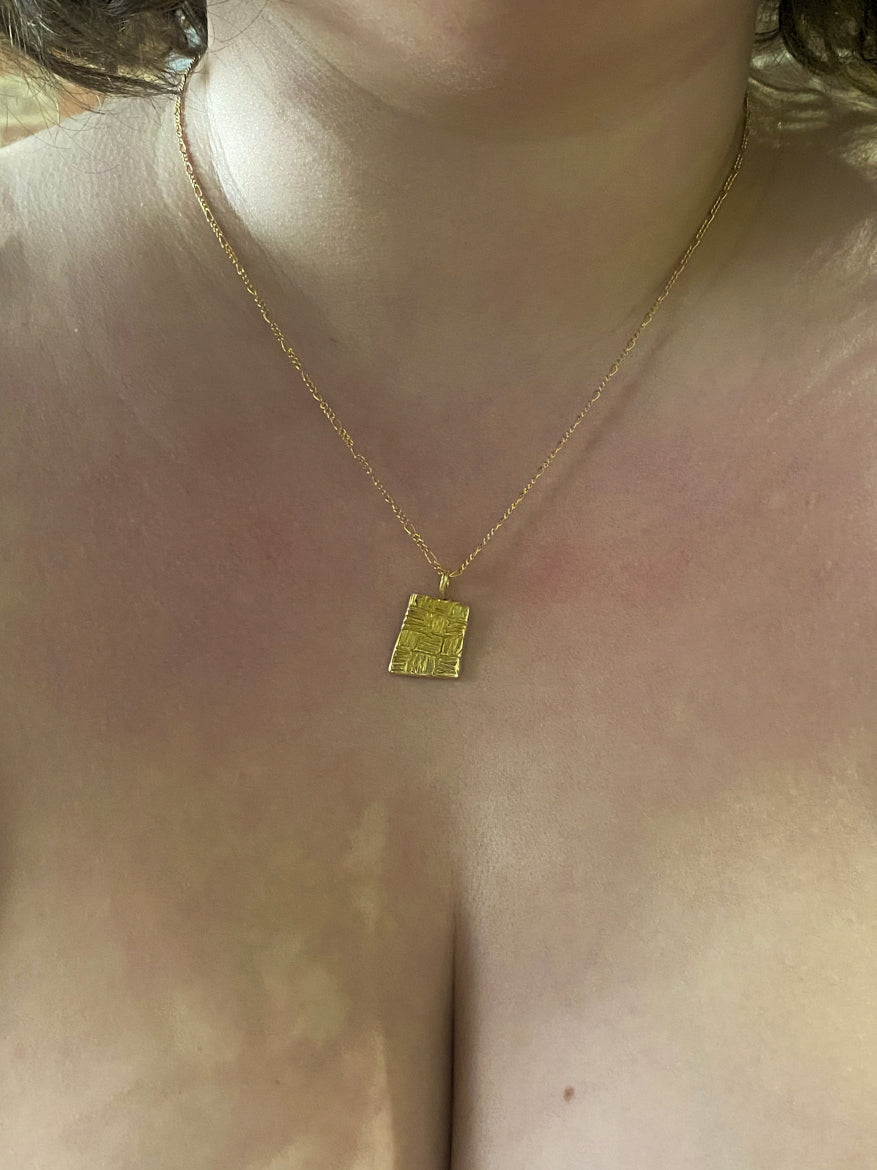 Gold rectangular pendant with checker lines hanging on chain on model with short hair