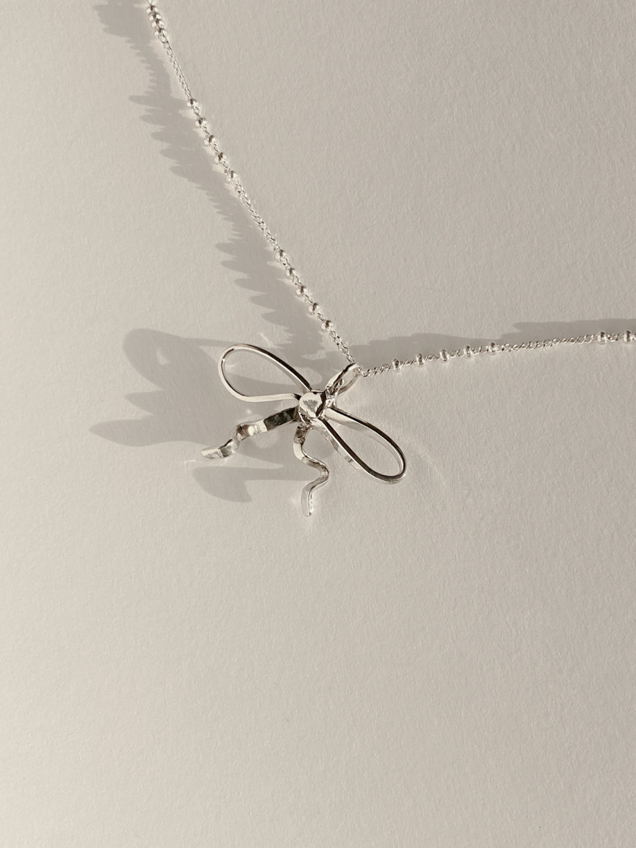 Sterling silver bow charm on chain with beads on white background