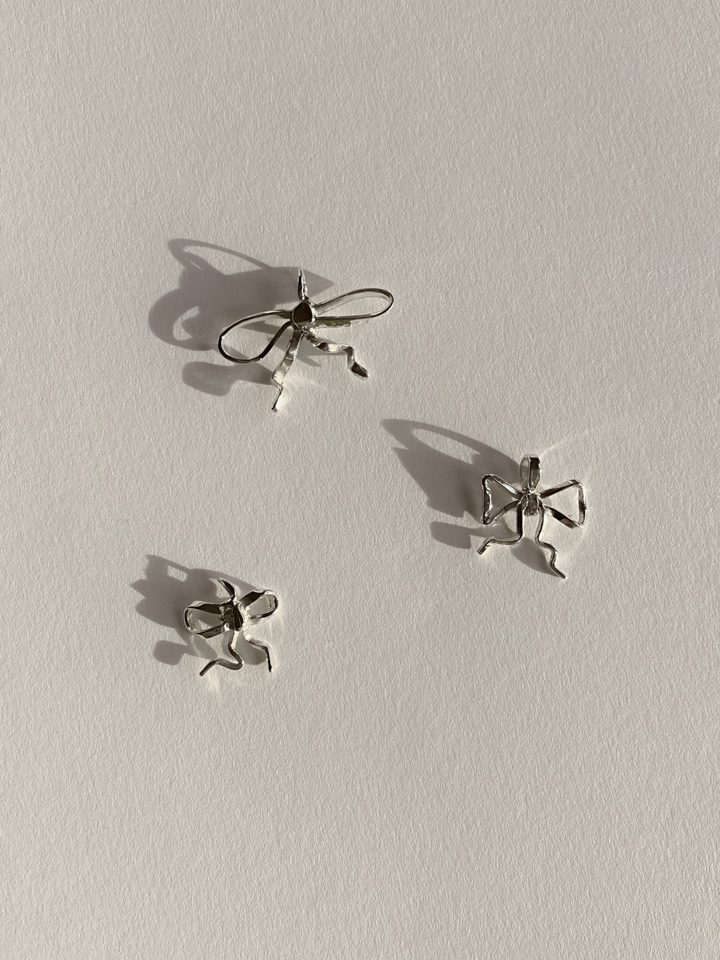 3 silver bow pendants on white background