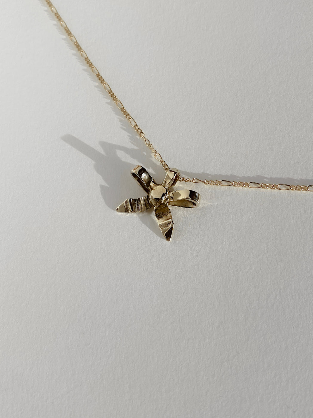 Gold bow ribbon charm on chain on white bacckground