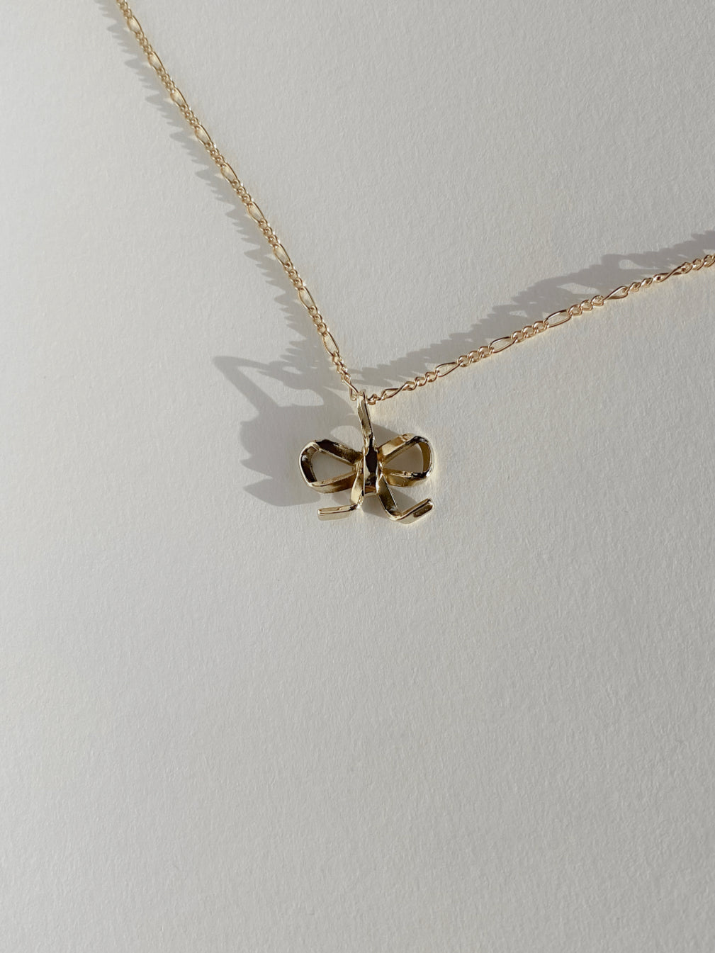 Gold bow charm necklace on white background