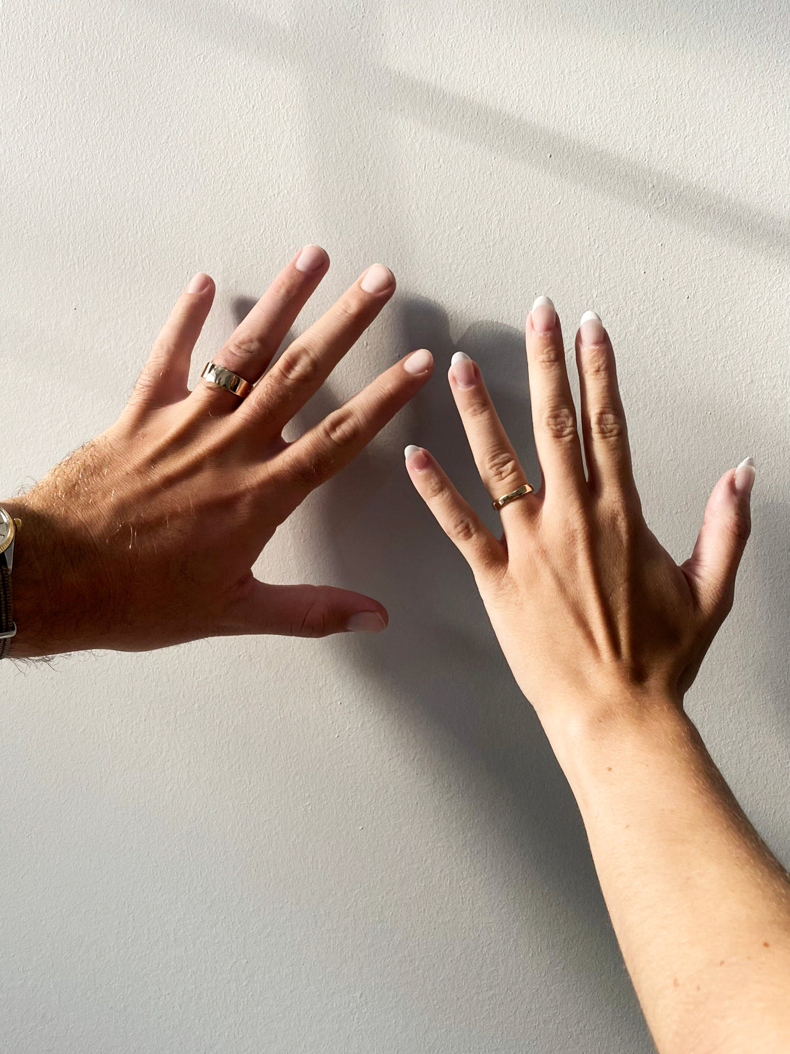 Two hands each with a wedding ring on in front of white wall
