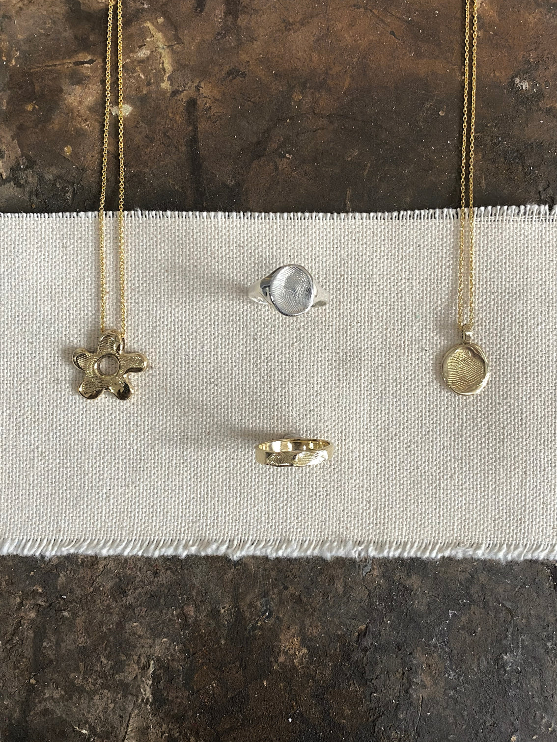Selection of 2 pendants and 2 rings with fingerprints cast in the surface, on canvas fabric
