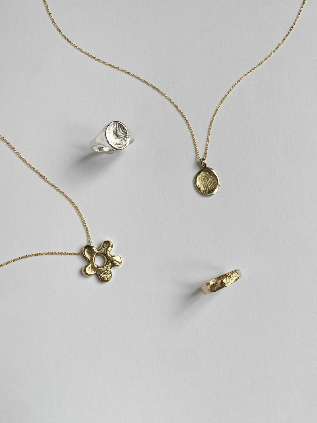 Selection of 2 pendants and 2 rings with fingerprints pressed into surface on white background