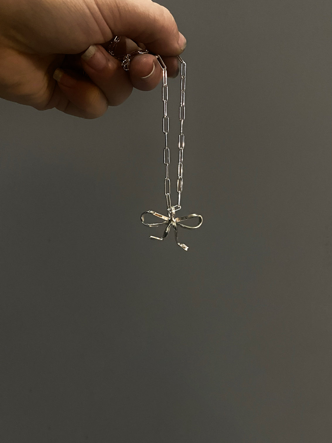 Medium silver bow pendant on chain with large oval links in hand