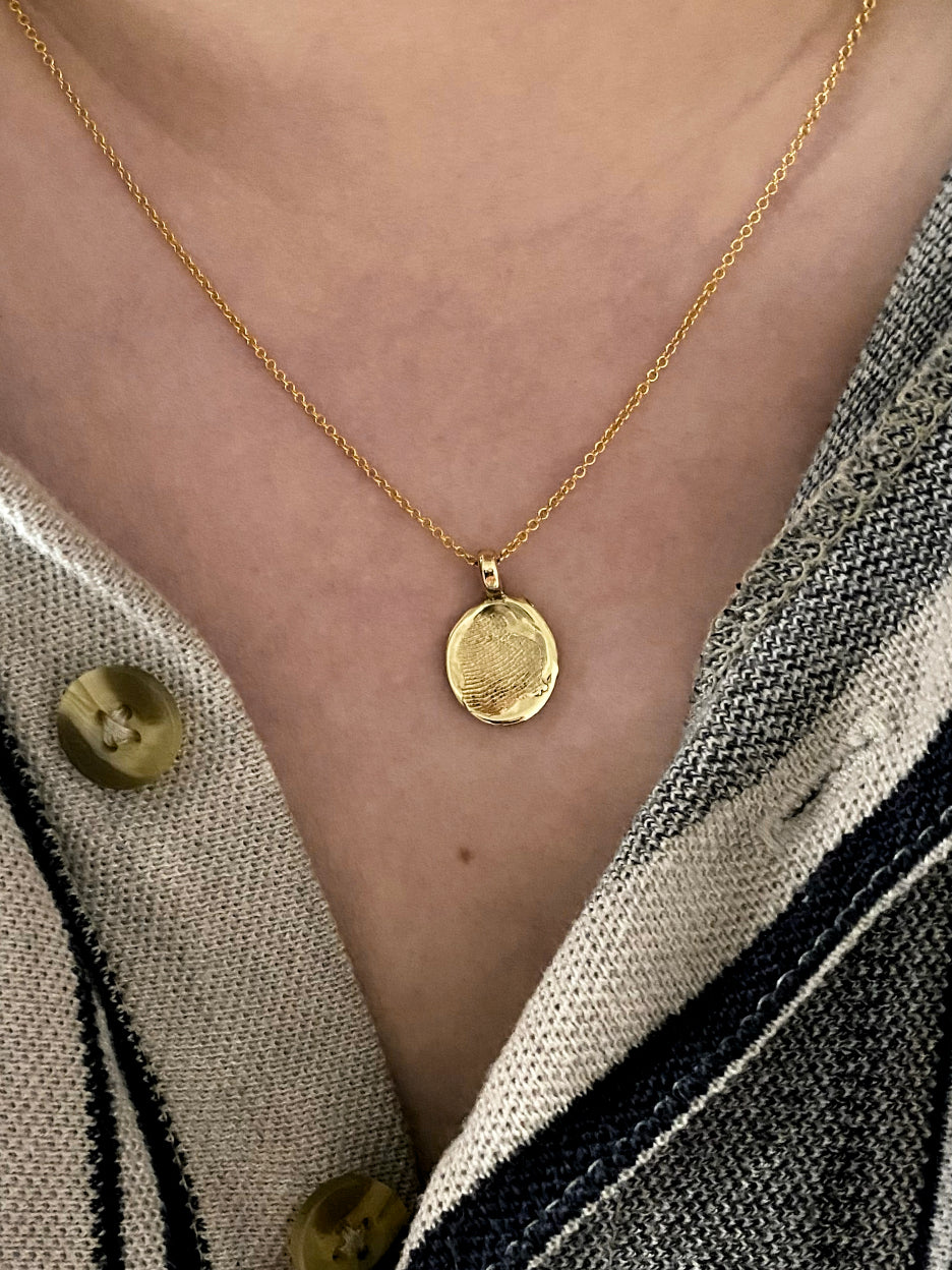 Gold fingerprint oval pendant on model with stripe black shirt