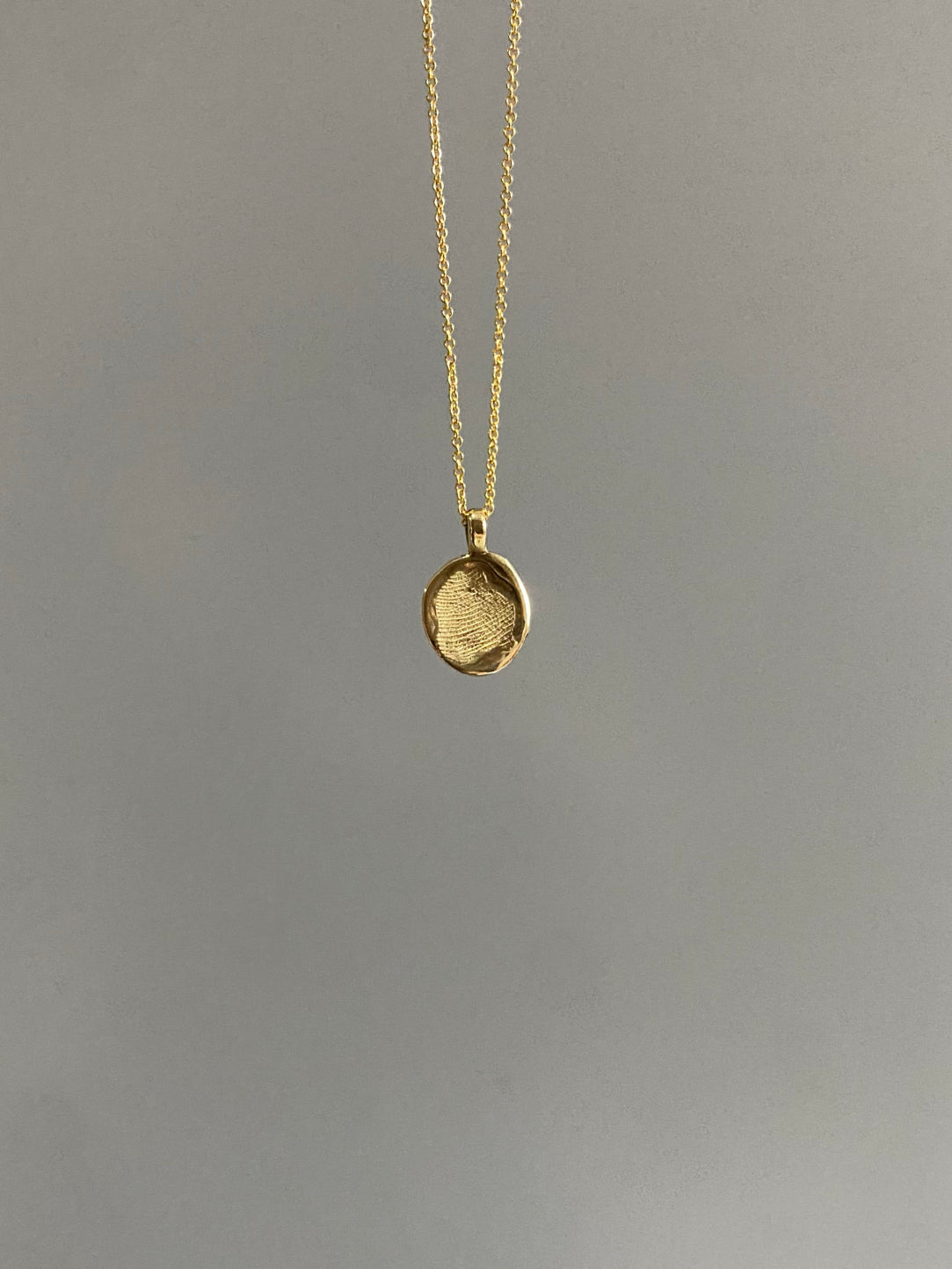 Gold oval necklace with fingerprint on surface on grey background