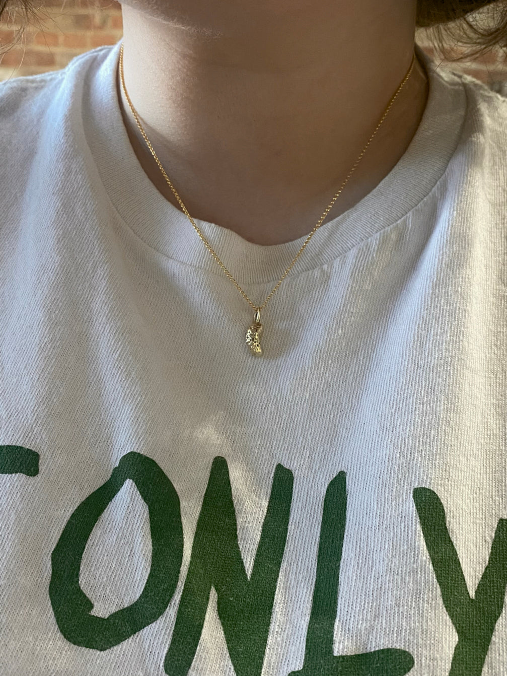 Gold pickle charm necklace on model with white tshirt
