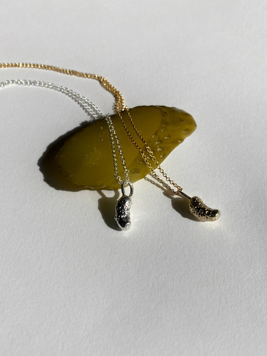 Silver and gold pickle charm necklaces resting on pickle slice on white background