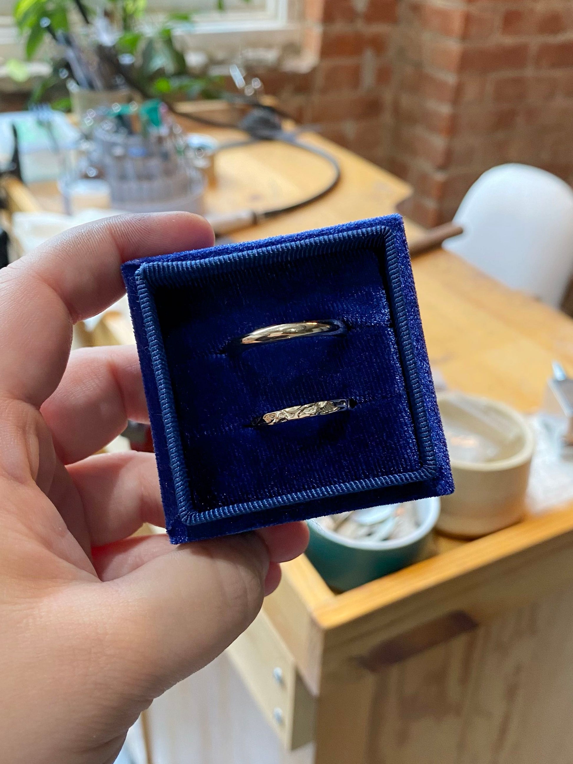 Two wedding rings in a blue box in front of jewellery work table
