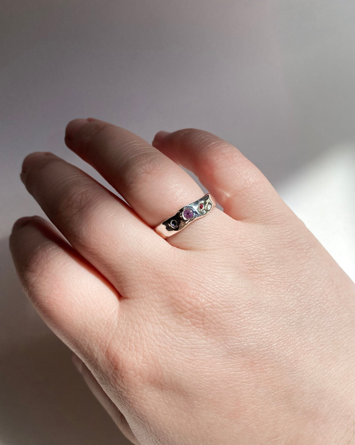 Molten silver ring with 1 blue, 1 red, and 1 pink sapphire on hand