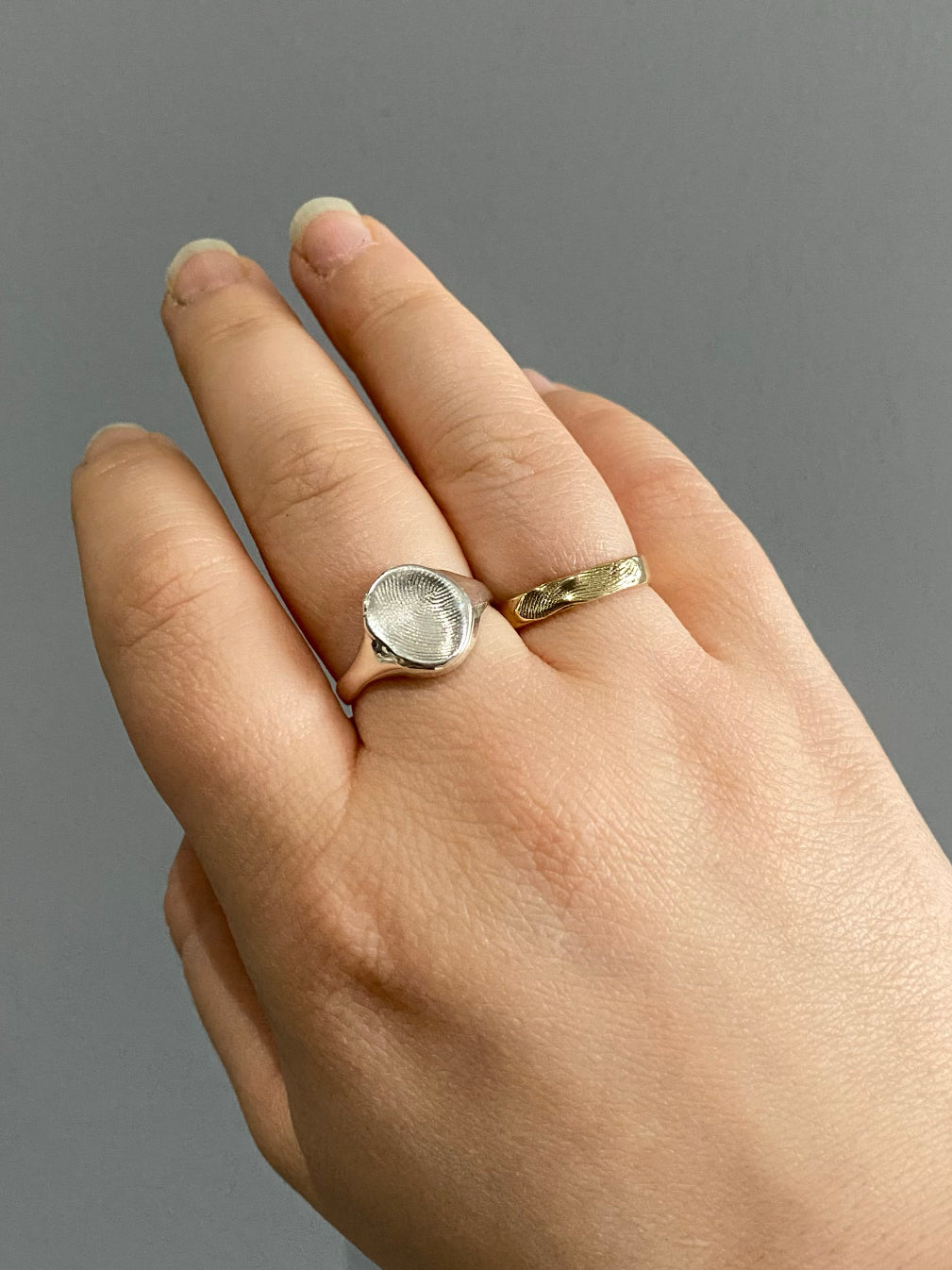 Hand with silver fingerprint signet ring and gold fingerprint band ring