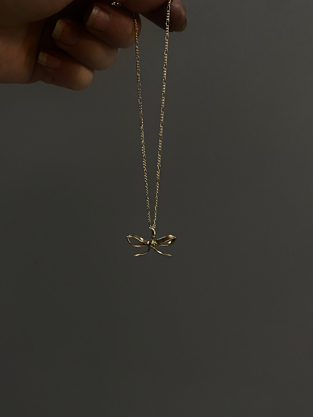 Small bow pendant necklace hanging from hand
