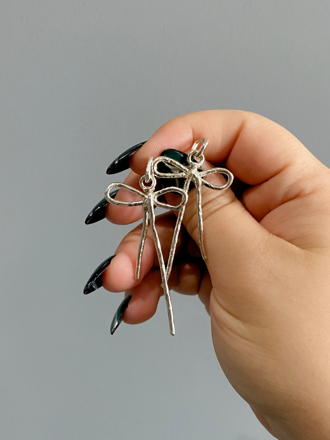 Sterling silver bow earrings in hand with long nails