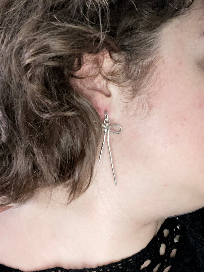 Sterling silver bow earrings on model with curly hair