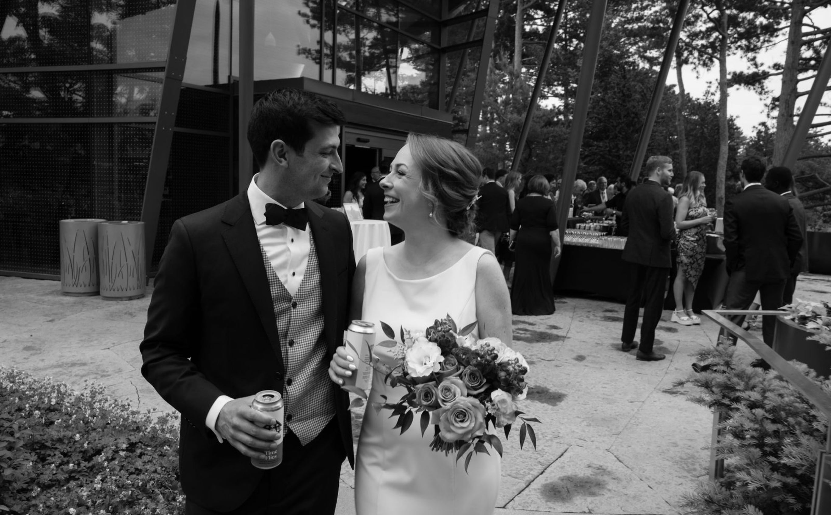 Couple with bouquet and beers at outdoor wedding in black and white