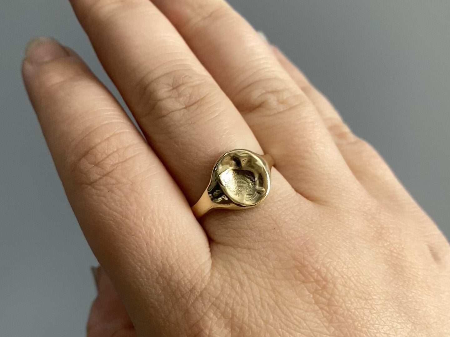 Load video: Hand with middle finger wearing oval signet ring with fingerprint pressed into the top
