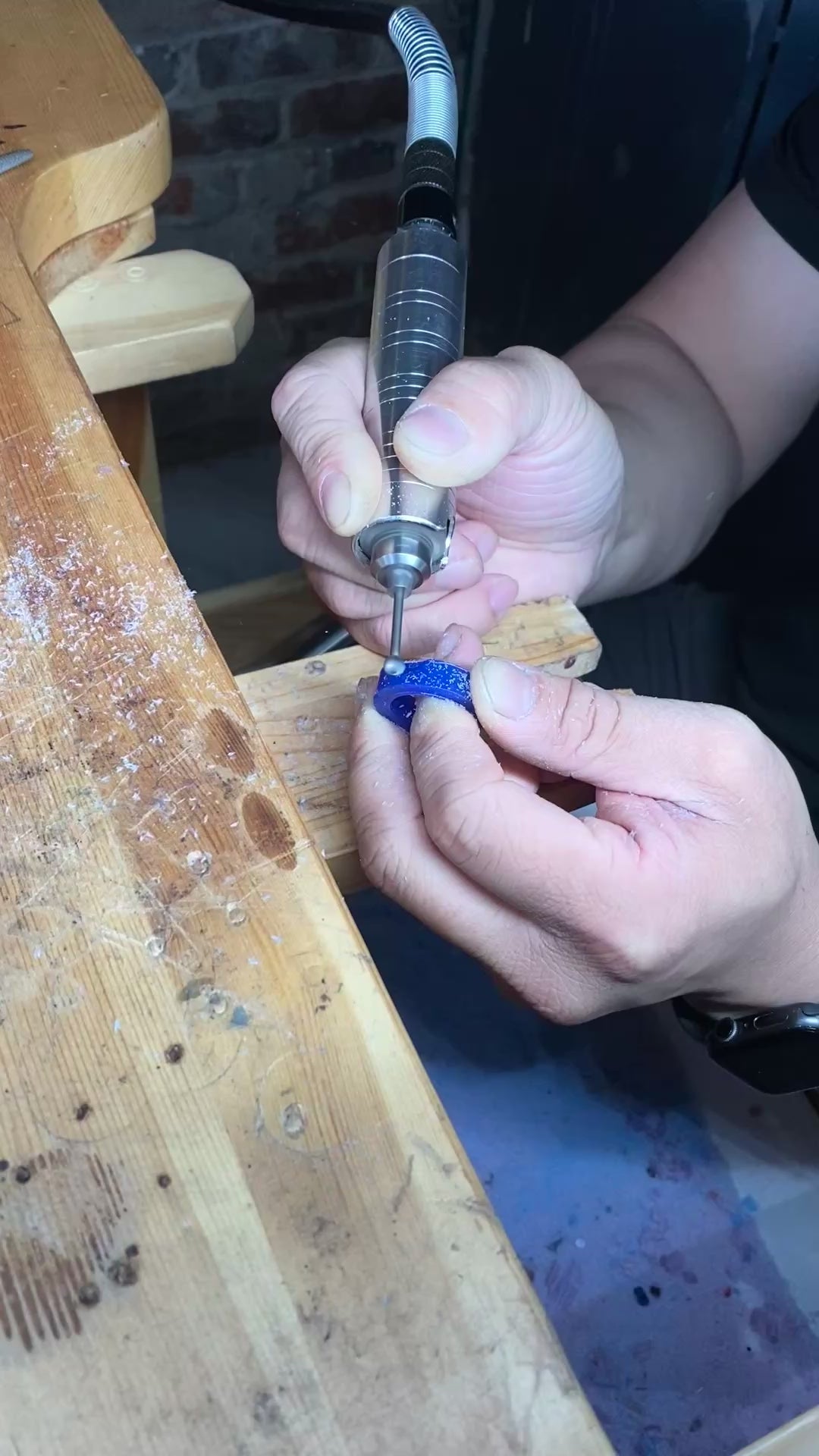 Load video: Person working at goldsmith bench holding a drill and removing wax from wax piece to form their ring