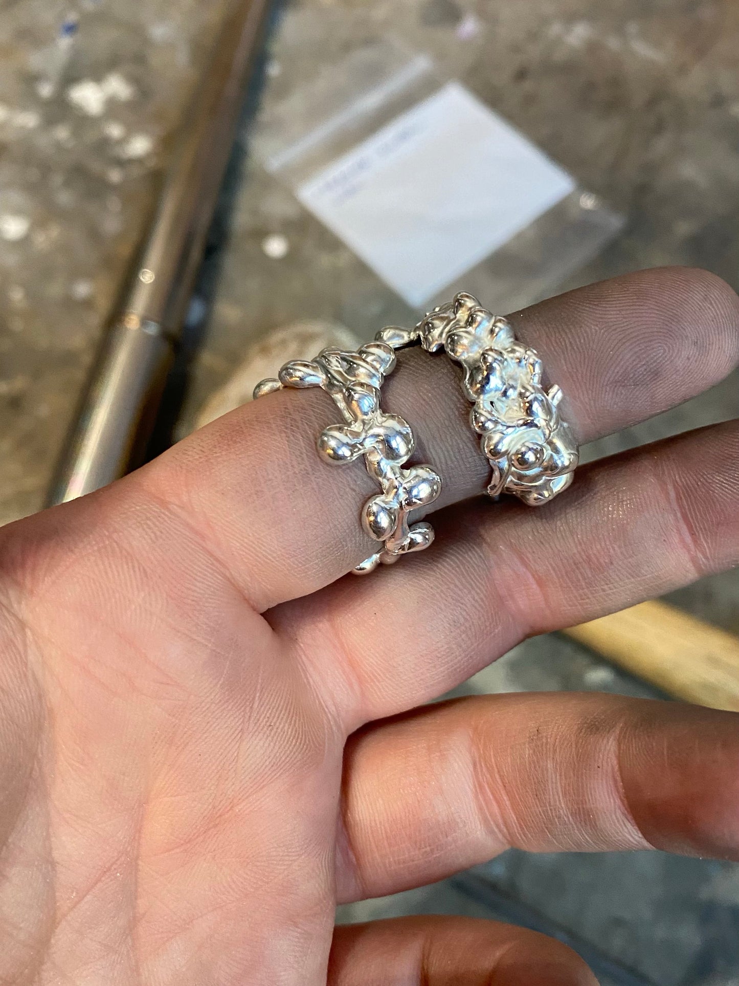 Two molten silver rings on hand in front of goldsmith tools