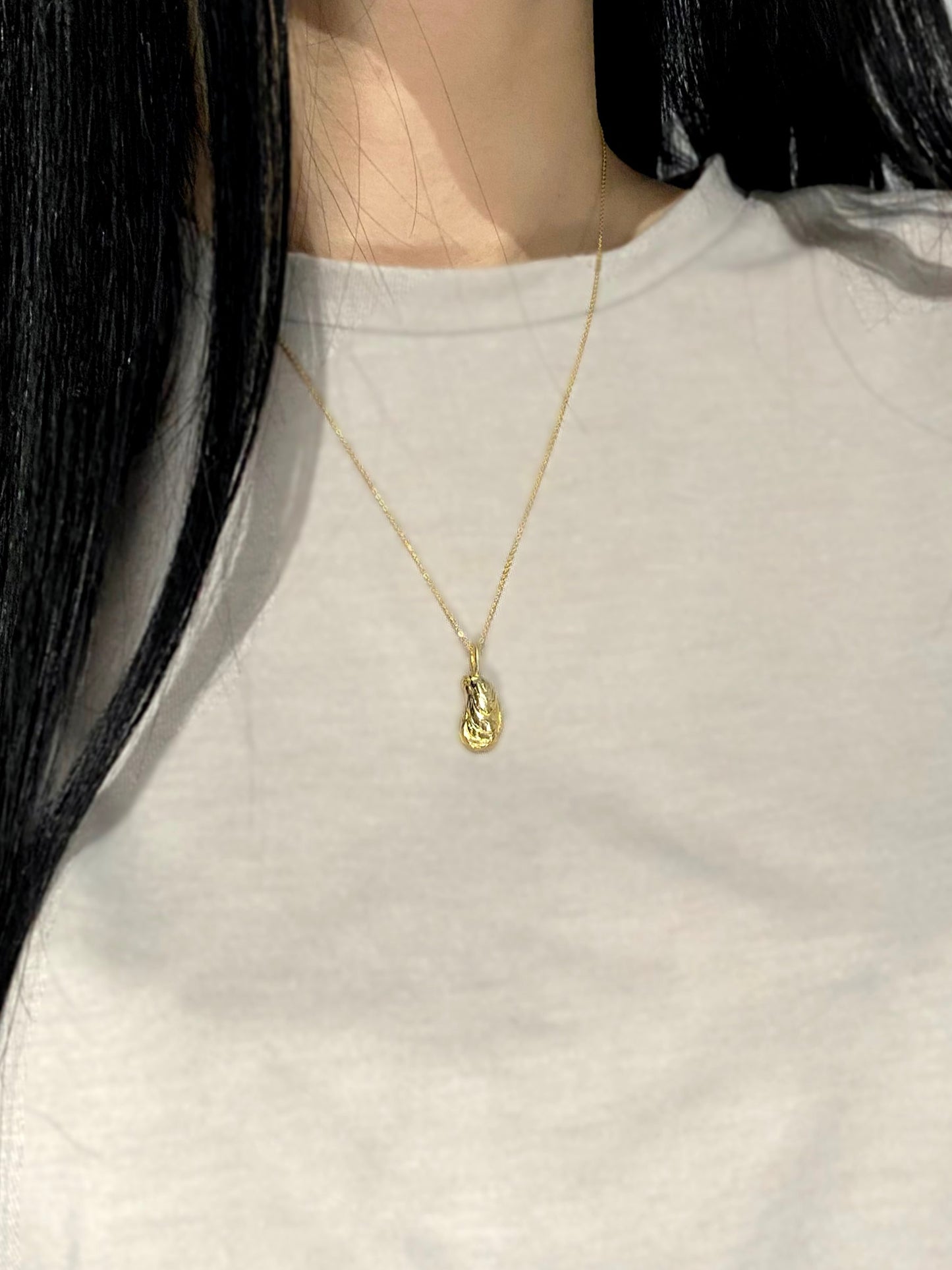 Gold oyster charm necklace on model with grey shirt