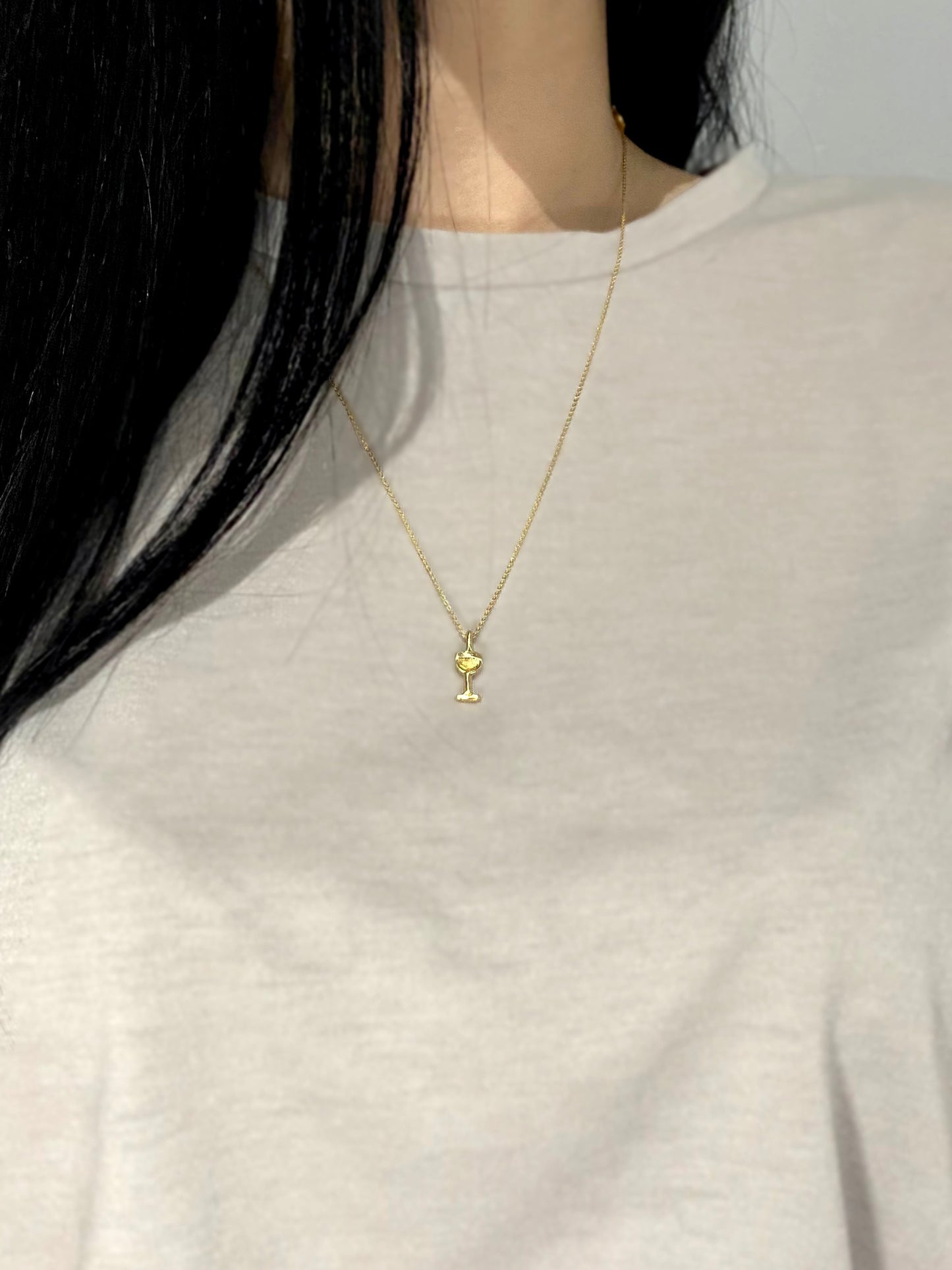 Gold wine glass necklace on model with grey shirt