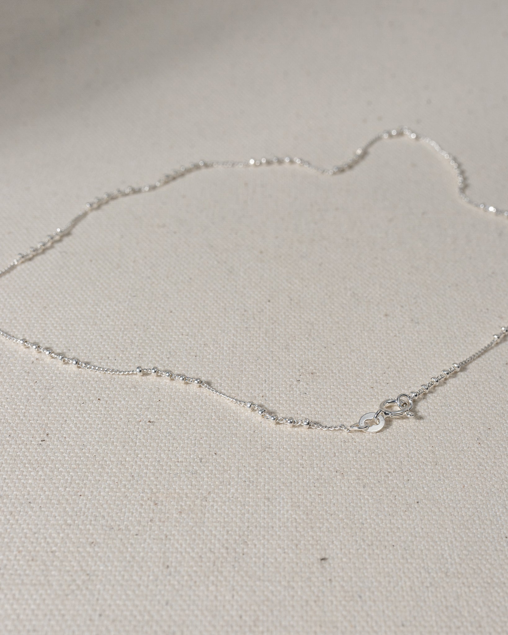 Silver chain with segments of 5 silver beads laying on canvas