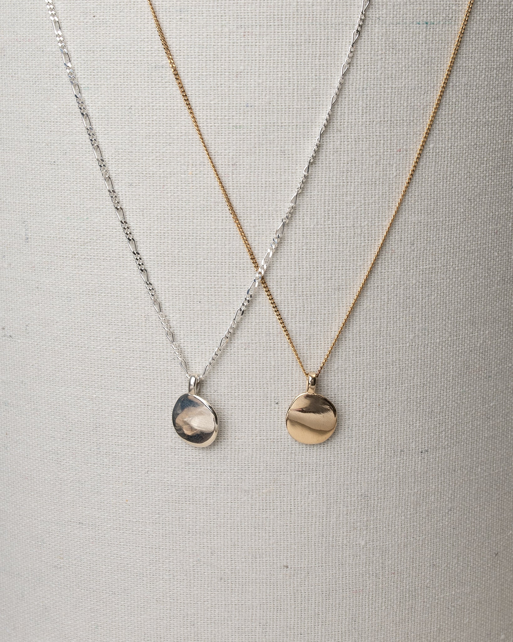 Silver and gold oval pendant necklaces hanging on canvas