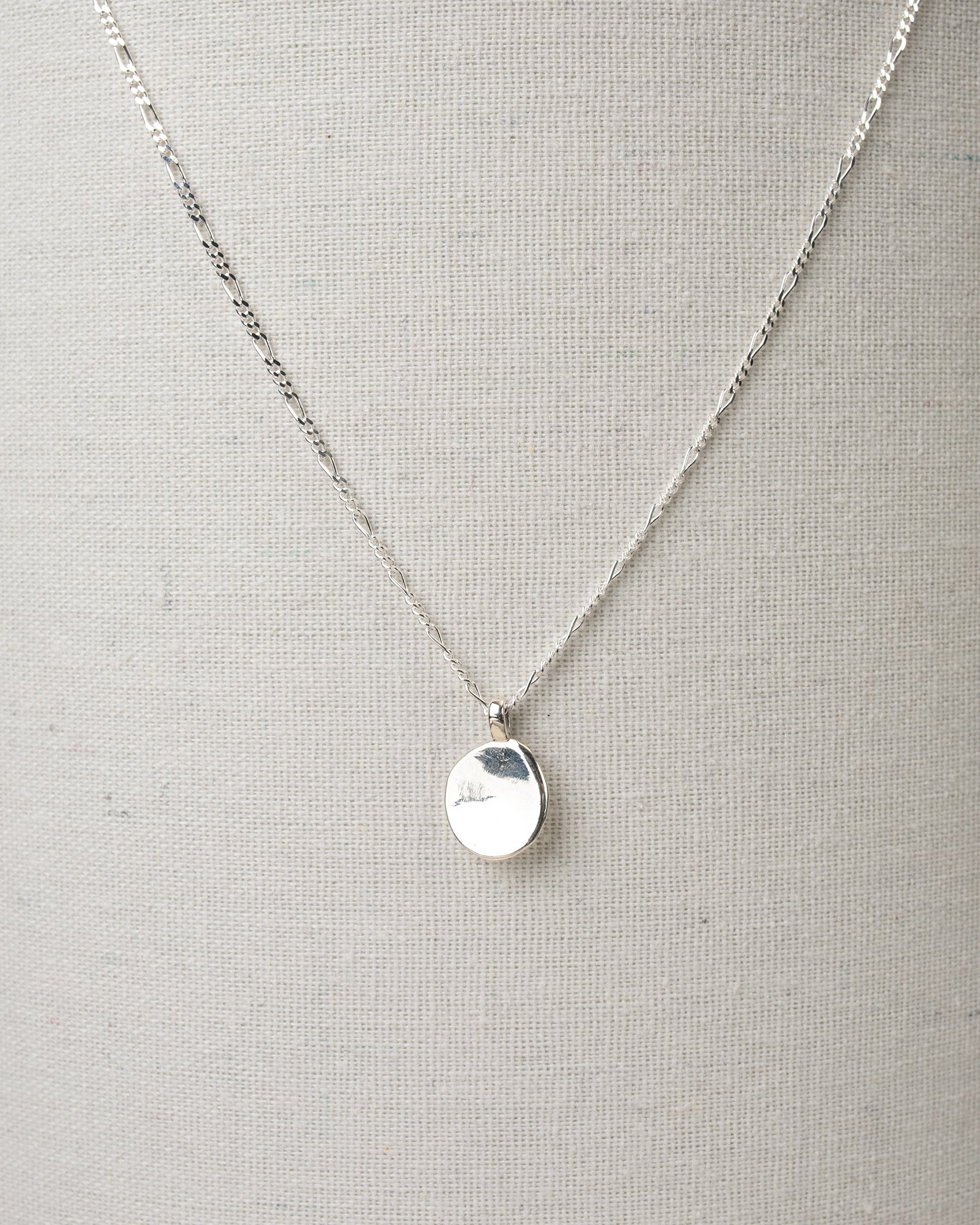Silver oval pendant necklace hanging on canvas