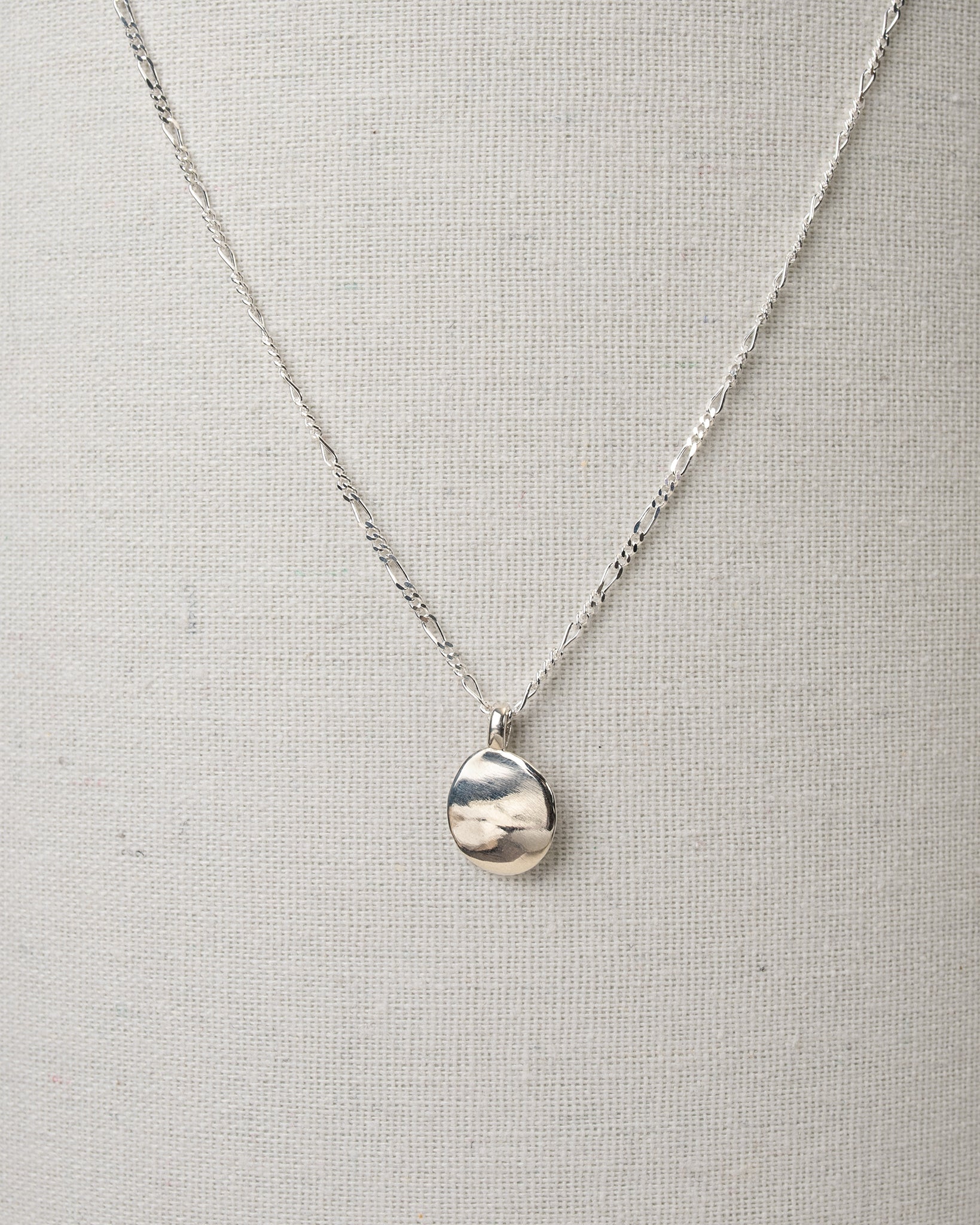 Silver oval pendant necklace hanging on canvas