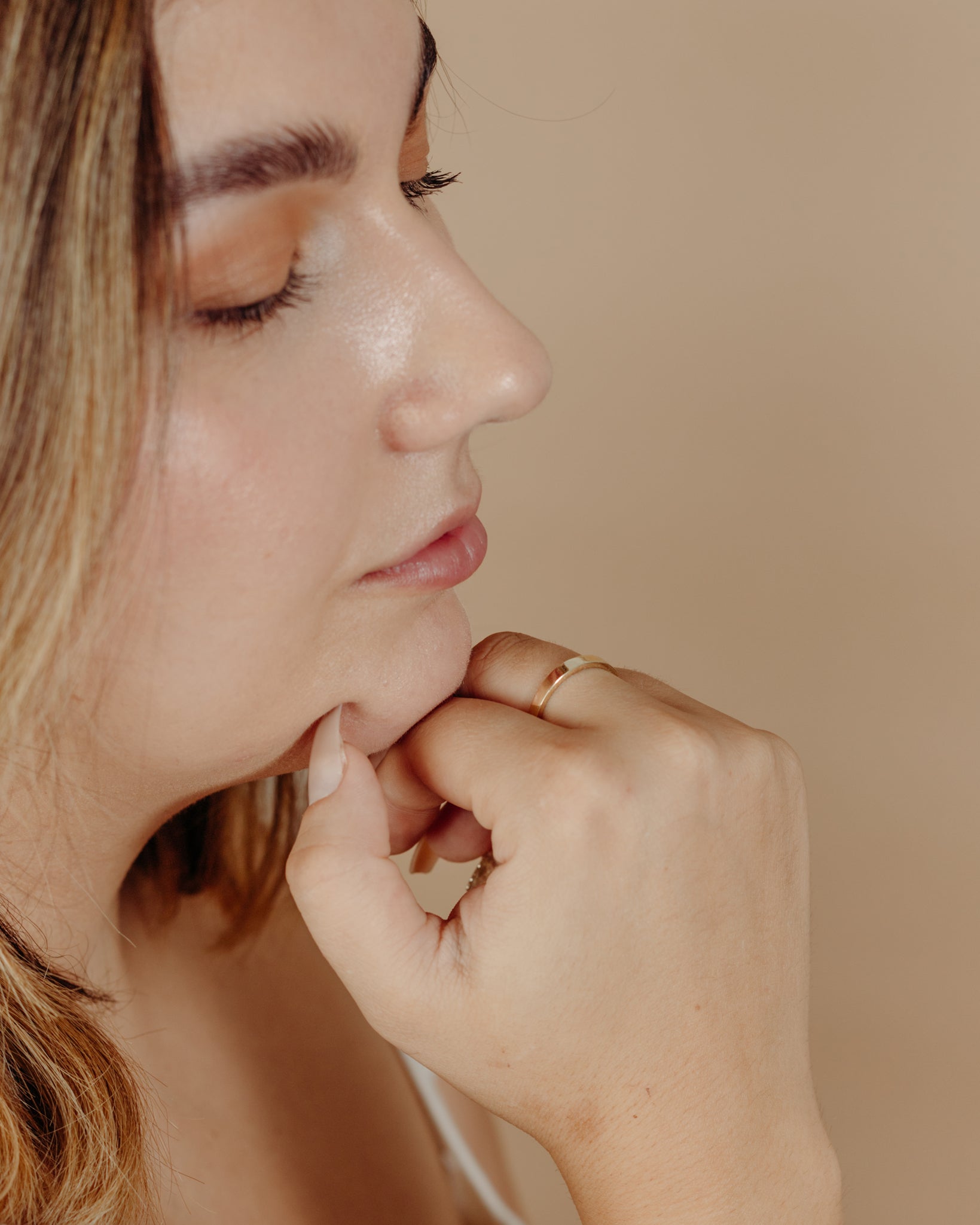 Simple flat gold ring on hand under model’s face